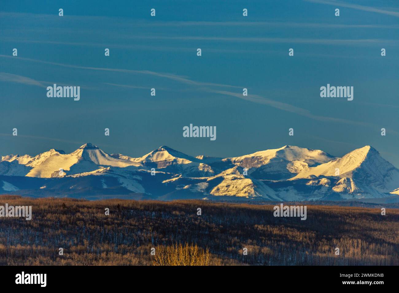 Catena montuosa innevata che si illumina di luce calda all'alba con le colline ai piedi e il cielo blu, a ovest di Calgary, Alberta; Alberta, Canada Foto Stock