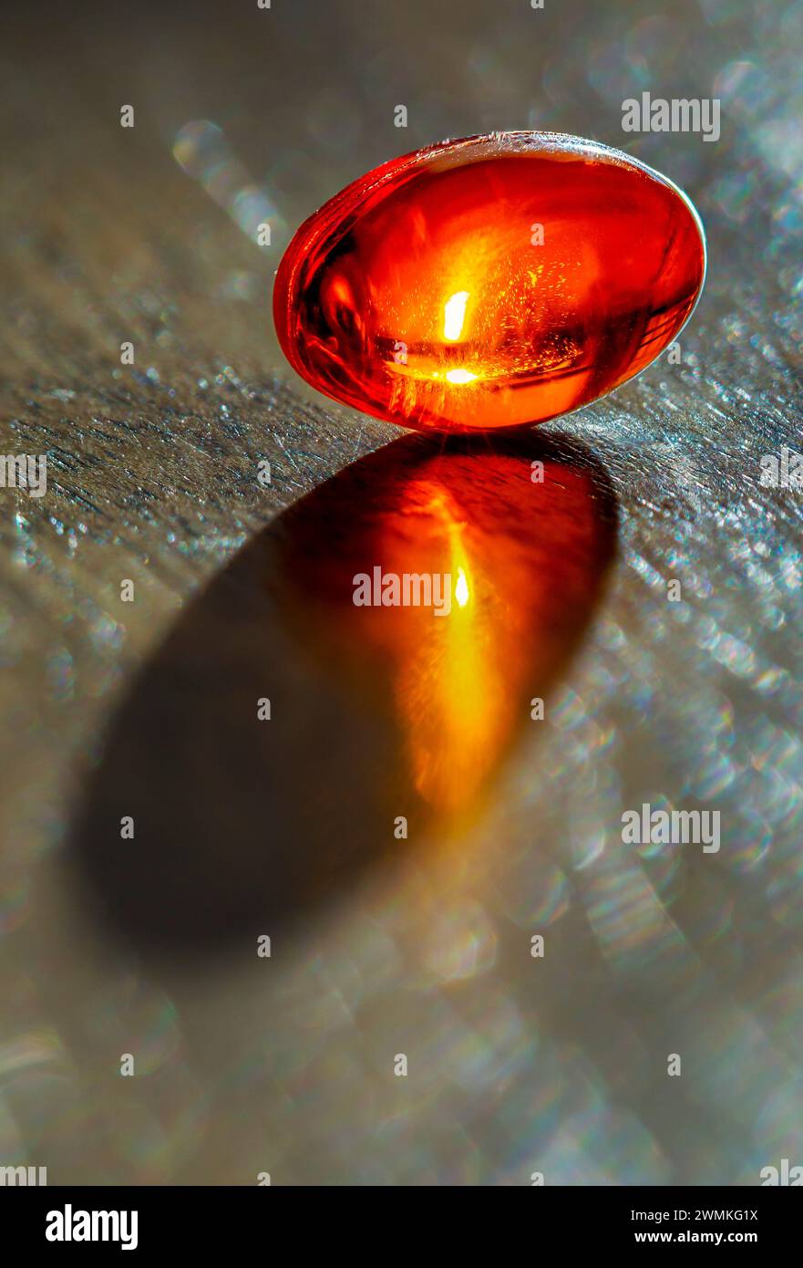 Primo piano di una capsula di gel luminoso con un bagliore solare all'interno su uno sfondo grigio ardesia; Studio Shot Foto Stock