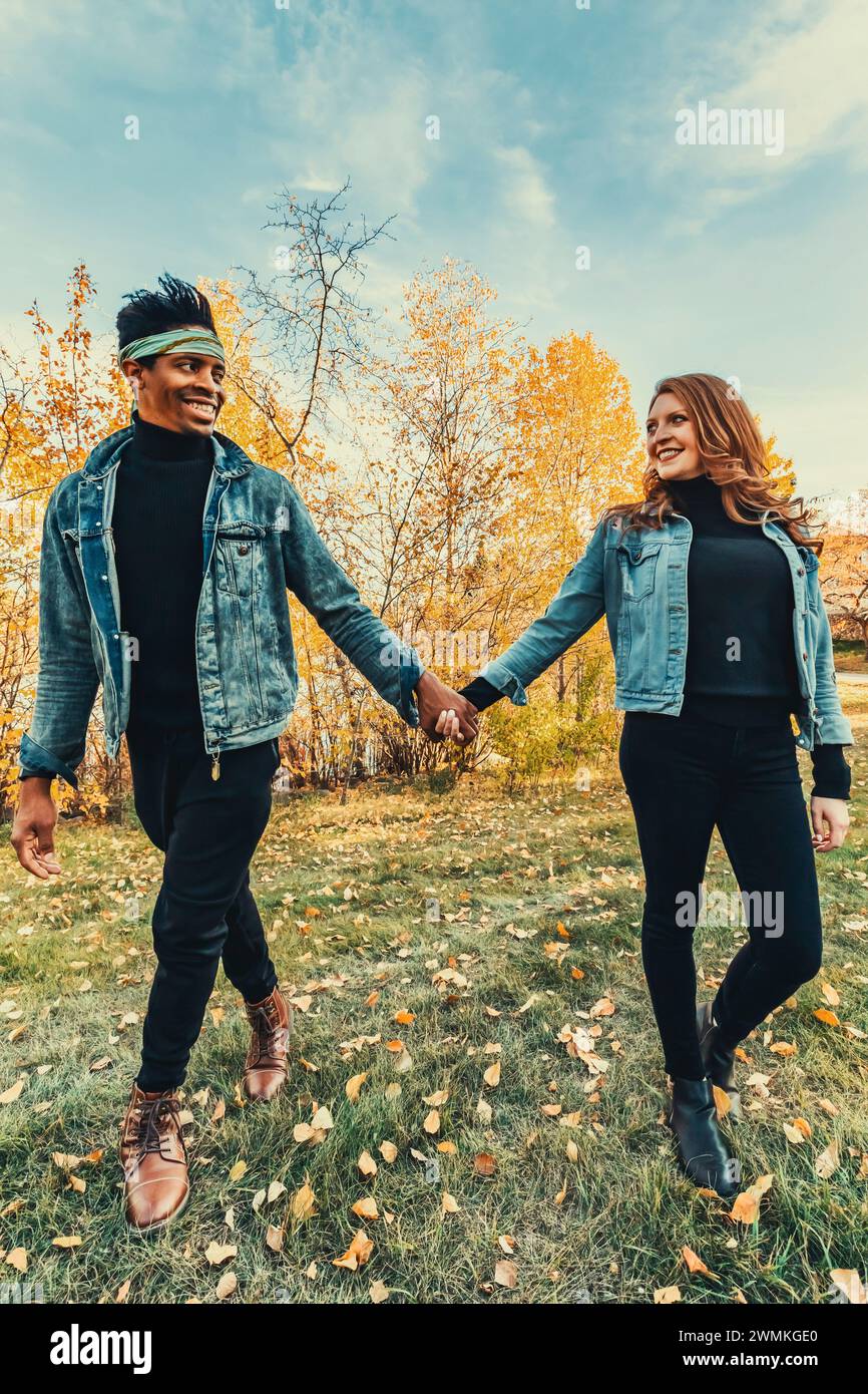 Coppia di sposi con corse miste sorridenti, camminando in un parco cittadino durante un'uscita di famiglia autunnale, trascorrendo del tempo di qualità insieme Foto Stock