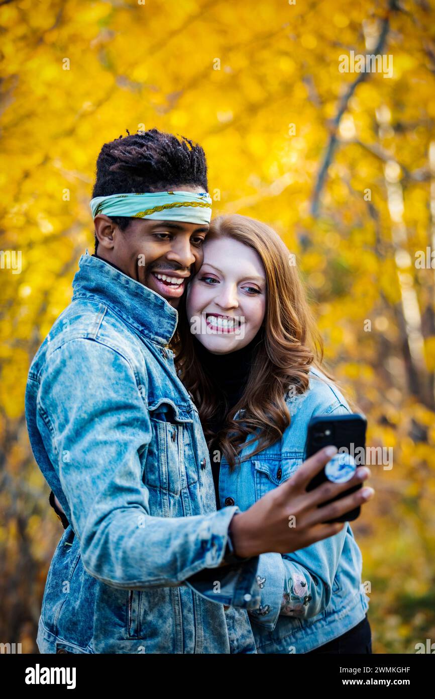 Primo piano di una coppia di sposi in gara mista che si fanno un selfie insieme, sorridono alla fotocamera del cellulare, trascorrono del tempo insieme durante una festa autunnale... Foto Stock