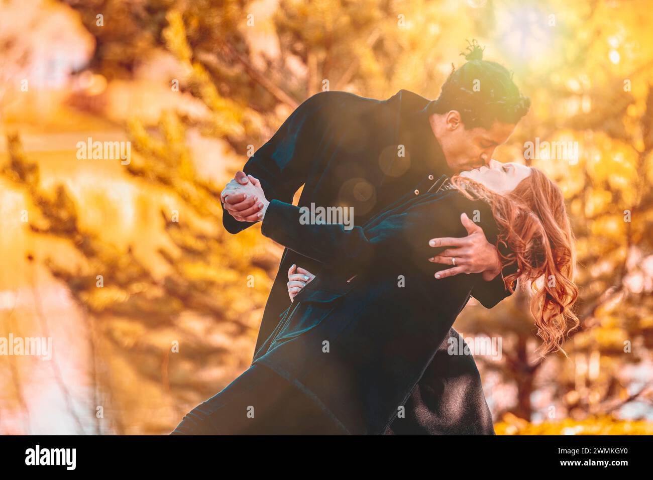 Una coppia di corse miste che si baciano mentre ballano e trascorrono del tempo insieme durante una gita in famiglia autunnale in un parco cittadino; Edmonton, Alberta, Canada Foto Stock