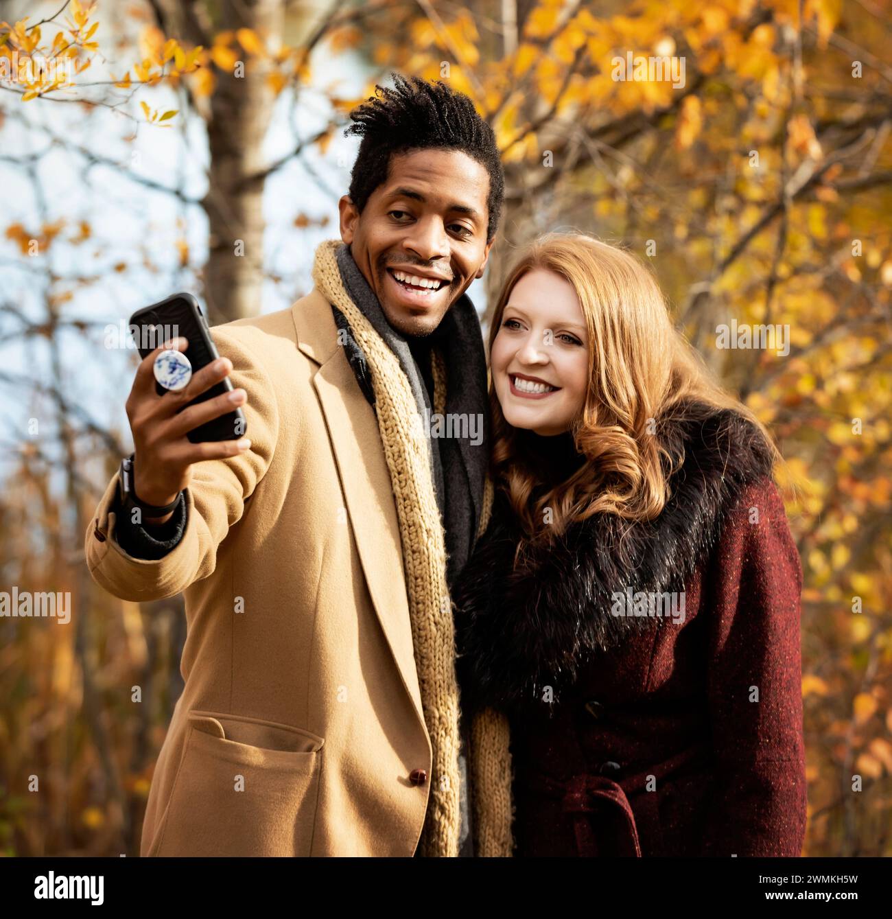 Primo piano di una coppia mista che si fa un selfie insieme, sorride alla fotocamera del cellulare, passa del tempo insieme durante una famiglia autunnale... Foto Stock
