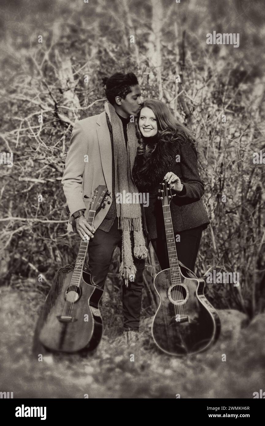 Ritratto di una coppia di sposi che tiene in mano chitarre acustiche mentre trascorre del tempo insieme durante una gita in famiglia autunnale in un parco cittadino Foto Stock