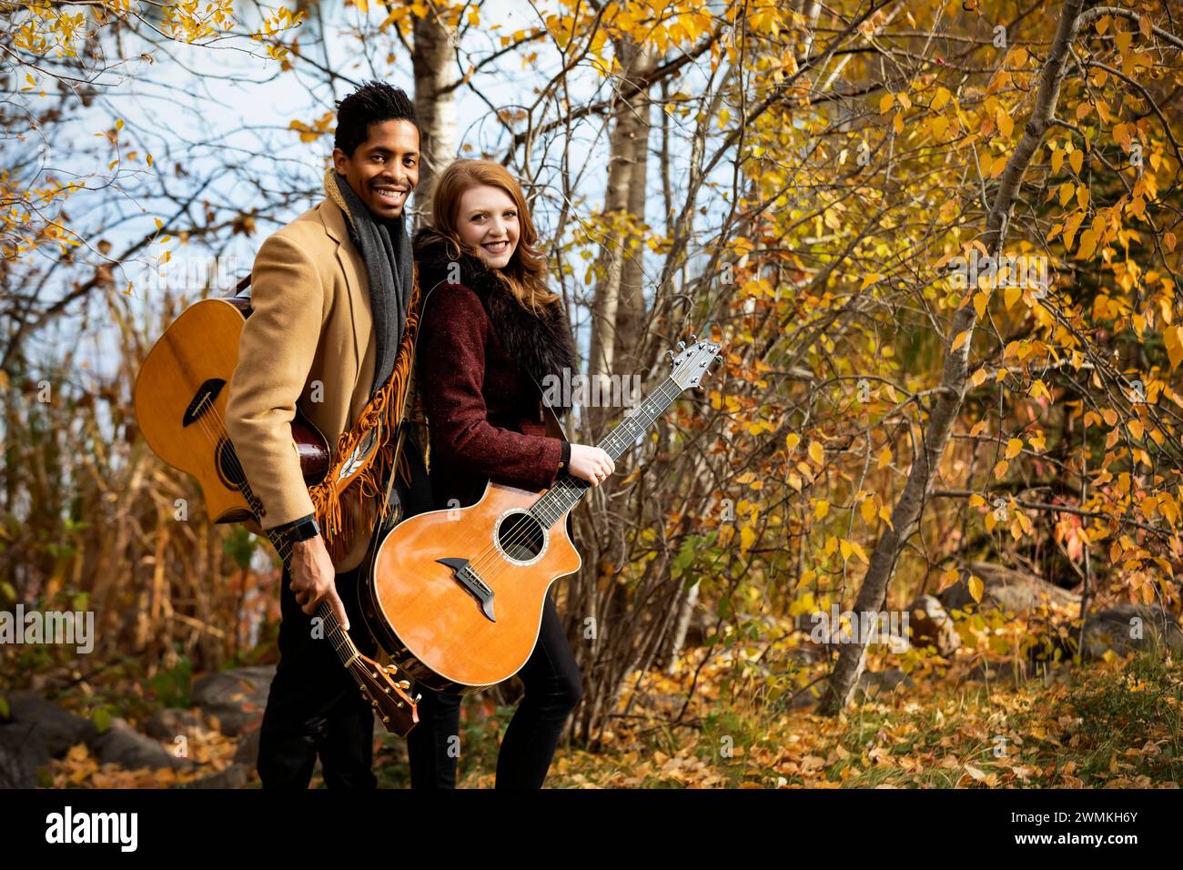 Ritratto di una coppia di coniugi che tiene in mano chitarre acustiche e sorride alla telecamera mentre trascorrono del tempo insieme durante un famil autunnale... Foto Stock