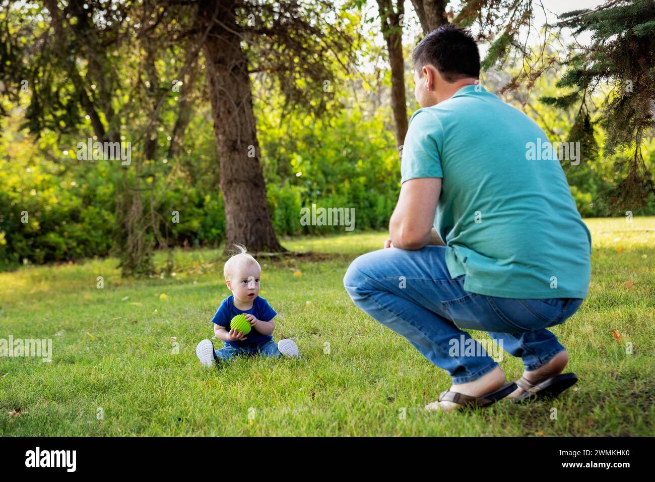 Padre trascorre del tempo di qualità e lancia una palla con suo figlio che ha la sindrome di Down, in un parco cittadino durante un caldo pomeriggio autunnale Foto Stock