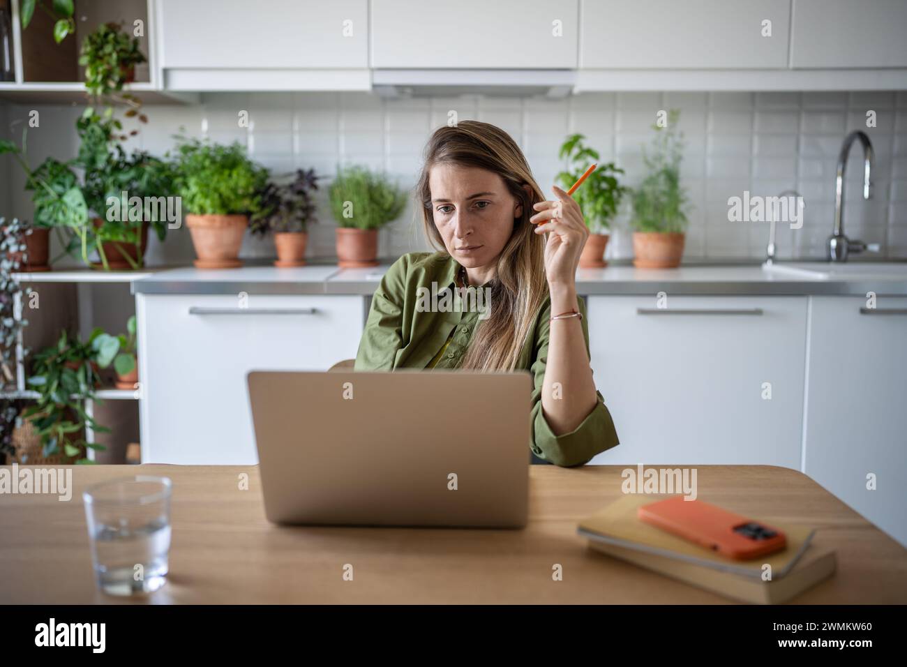 Donna impegnata e premurosa seduta in cucina, lavora freelance a casa, legge attentamente, pensa Foto Stock