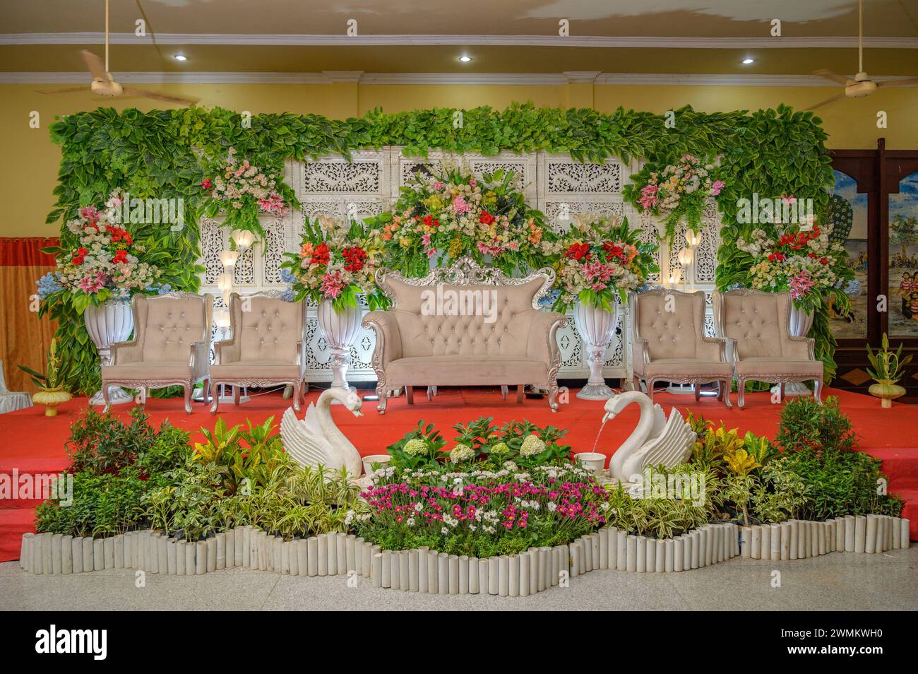 Decorazioni per matrimoni indonesiane con sfondo in legno decorato con fiori, lampadari e splendide sedie Foto Stock