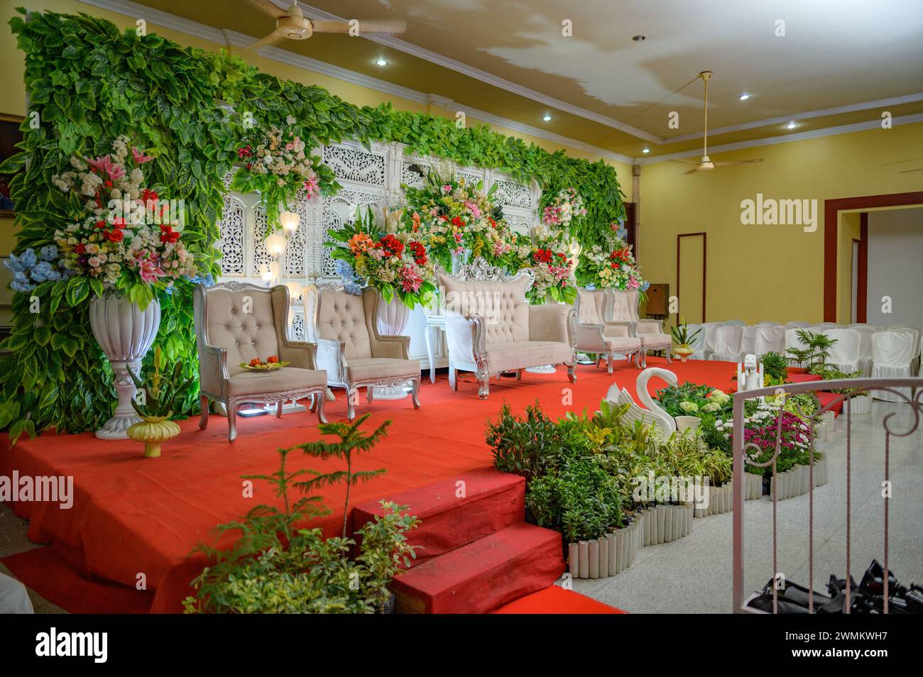 Decorazioni per matrimoni indonesiane con sfondo in legno decorato con fiori, lampadari e splendide sedie Foto Stock