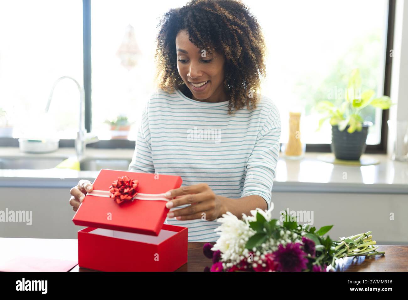 Una donna birazziale apre una confezione regalo a casa durante una videochiamata online Foto Stock