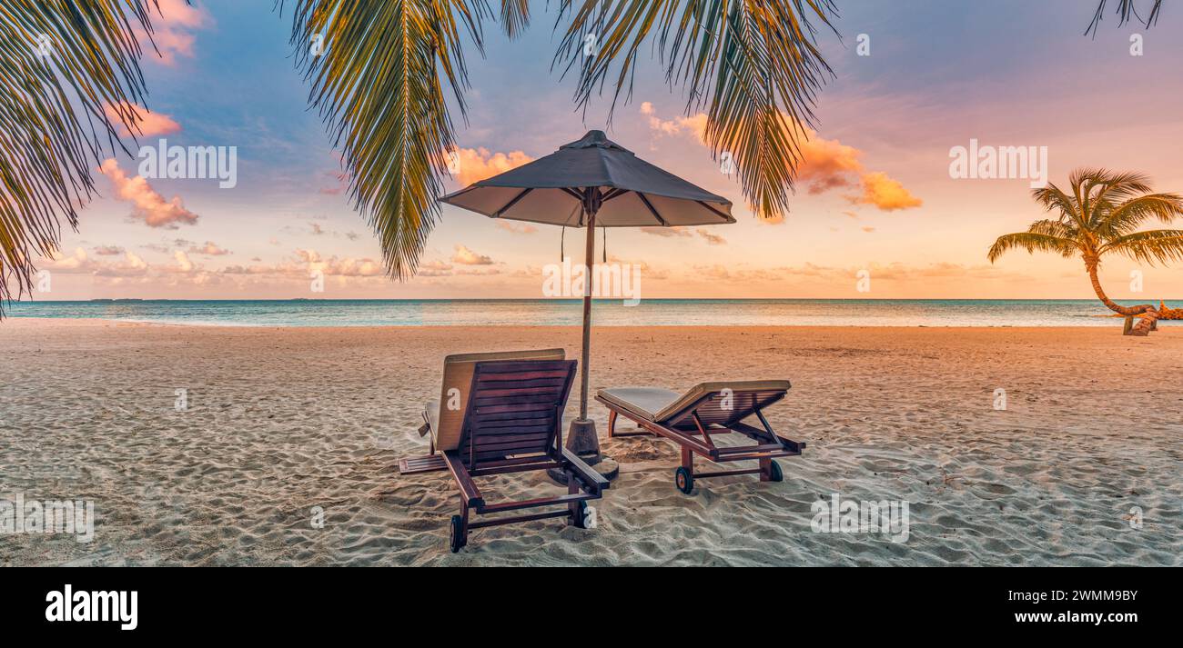 Splendida natura panoramica. Il tramonto sulla spiaggia tropicale mentre il paesaggio estivo dell'isola con sedie a sdraio, la palma lascia calmo mare e costa. Viaggi di lusso Foto Stock