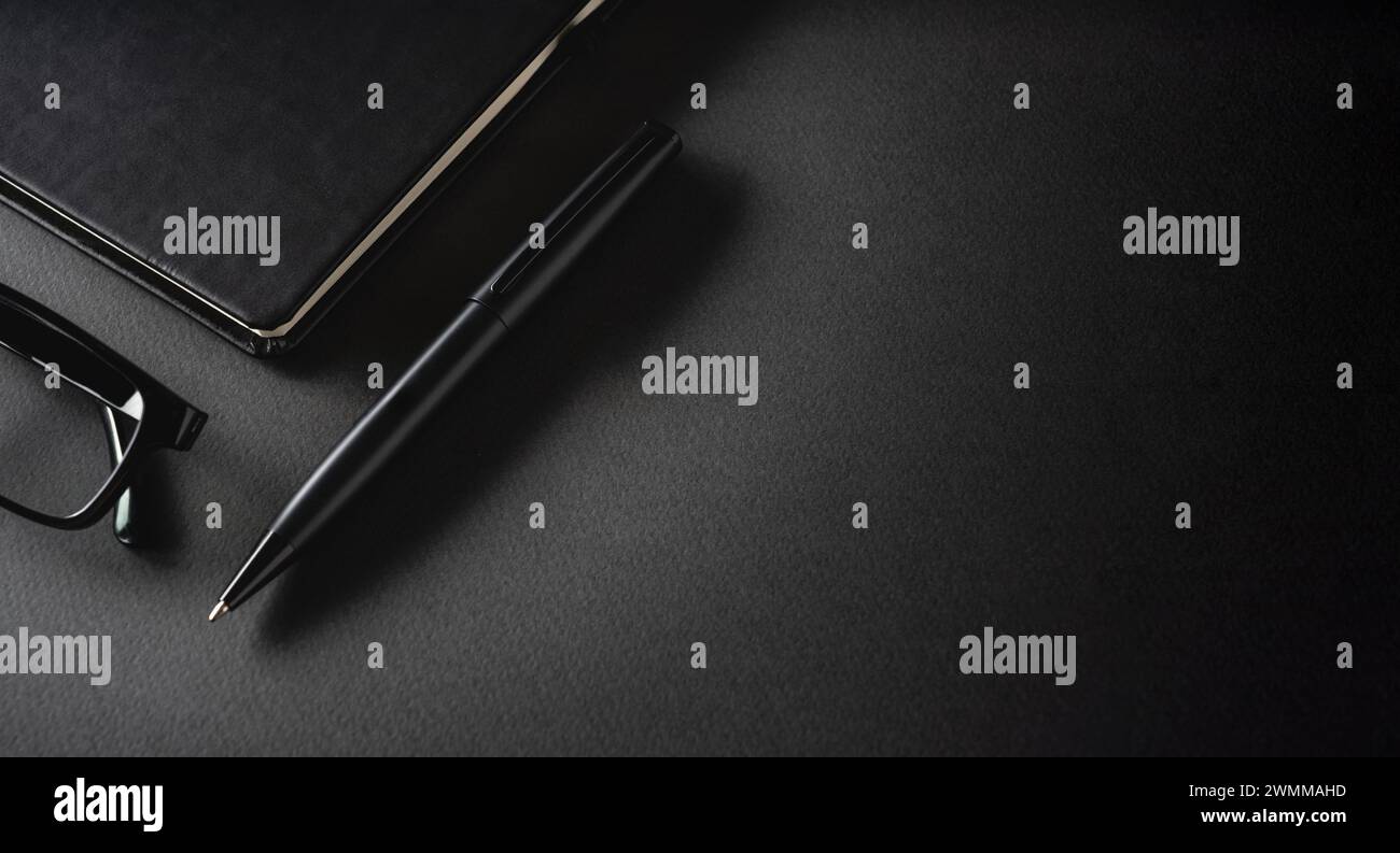 Vista dall'alto della penna a sfera, degli occhiali e del blocco note su un tavolo grigio scuro Foto Stock