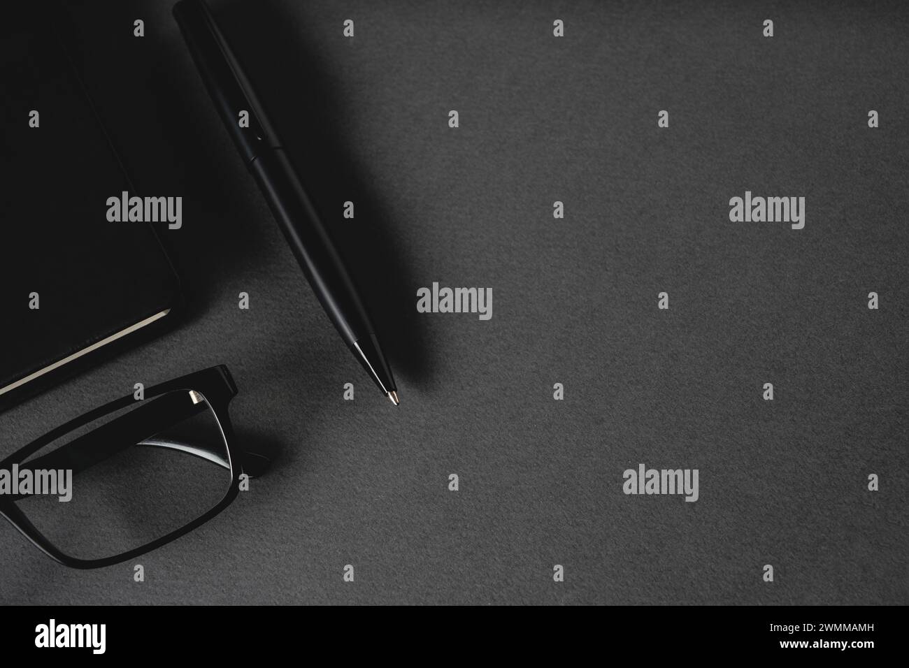 Vista dall'alto della penna a sfera, degli occhiali e del blocco note su un tavolo grigio scuro Foto Stock