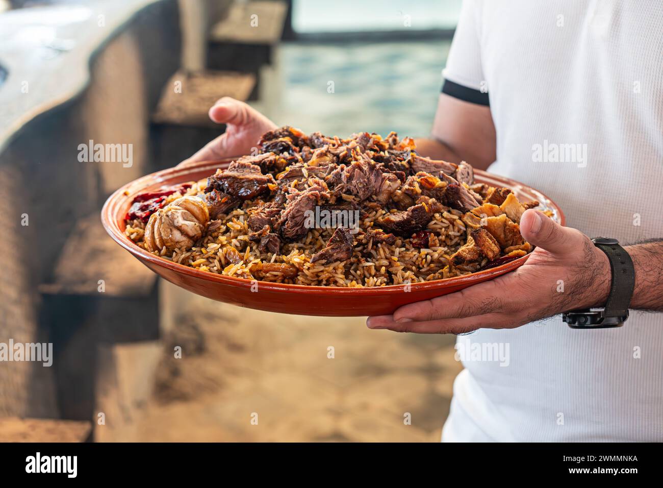Cibo nazionale - pilaf uzbeko con carne in piatto con schema tradizionale. il cameriere consegna il pilaf nel ristorante Foto Stock