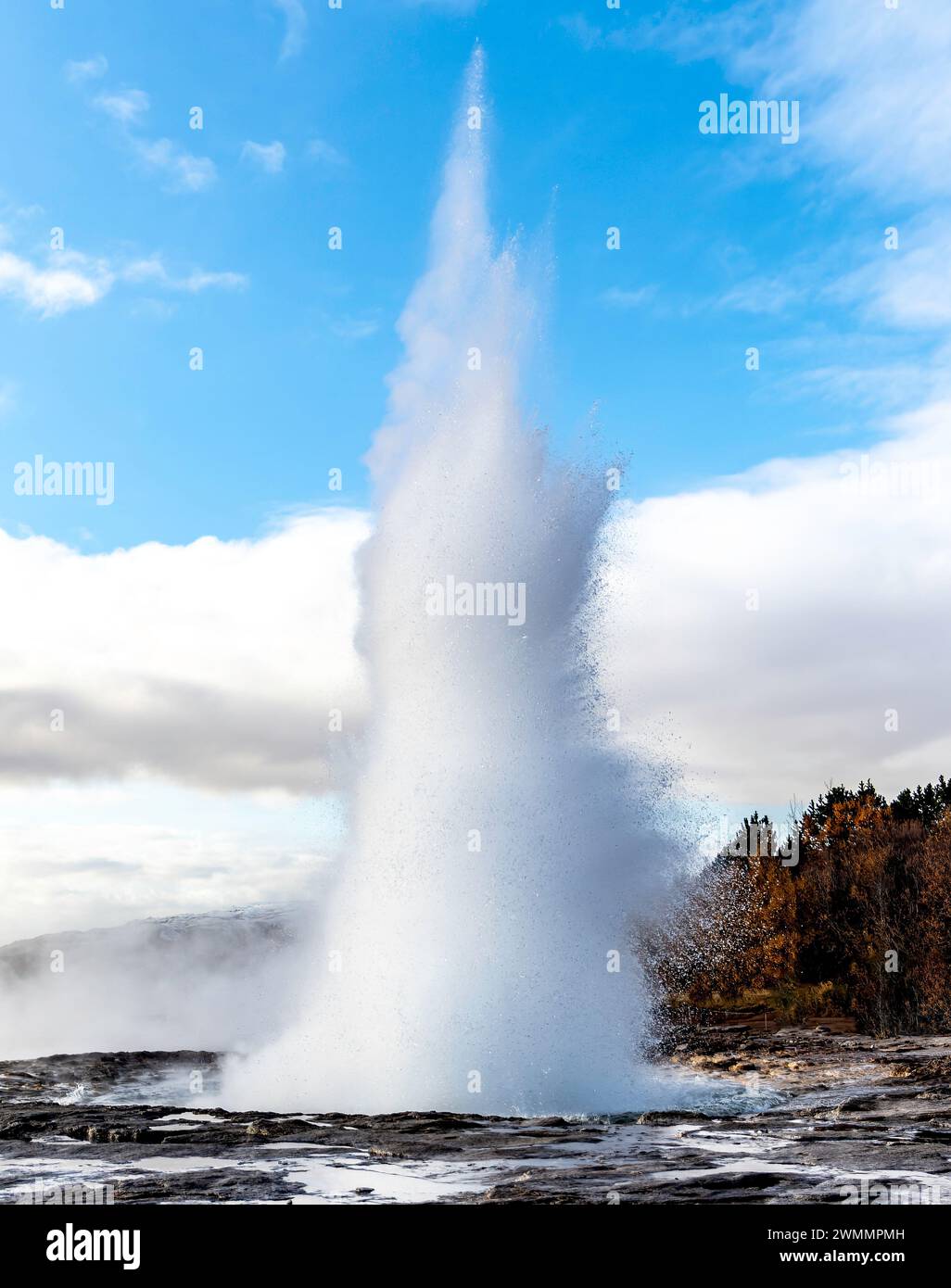 Pittoresco scenario di acqua sorgiva naturale dal terreno vulcanico geyser contro le montagne sotto il cielo azzurro nuvoloso alla luce del giorno. Smidur Geysi Foto Stock