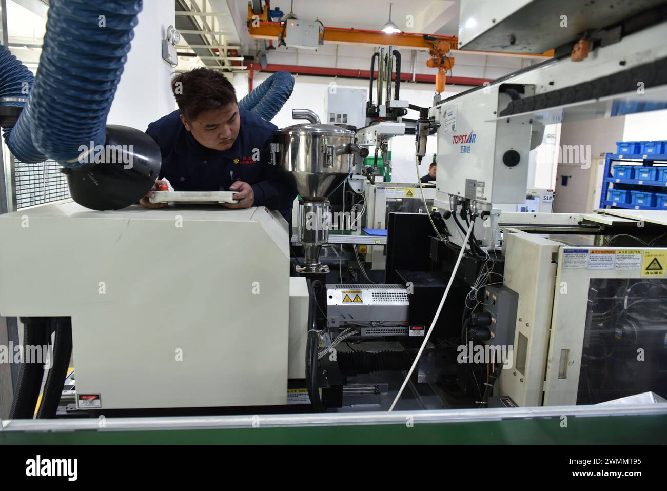 FUYANG, CINA - 27 FEBBRAIO 2024 - Un lavoratore gestisce una macchina per lo stampaggio a iniezione per produrre prodotti per lo stampaggio a iniezione di polveri metalliche a Fuyang, in Anhui Foto Stock