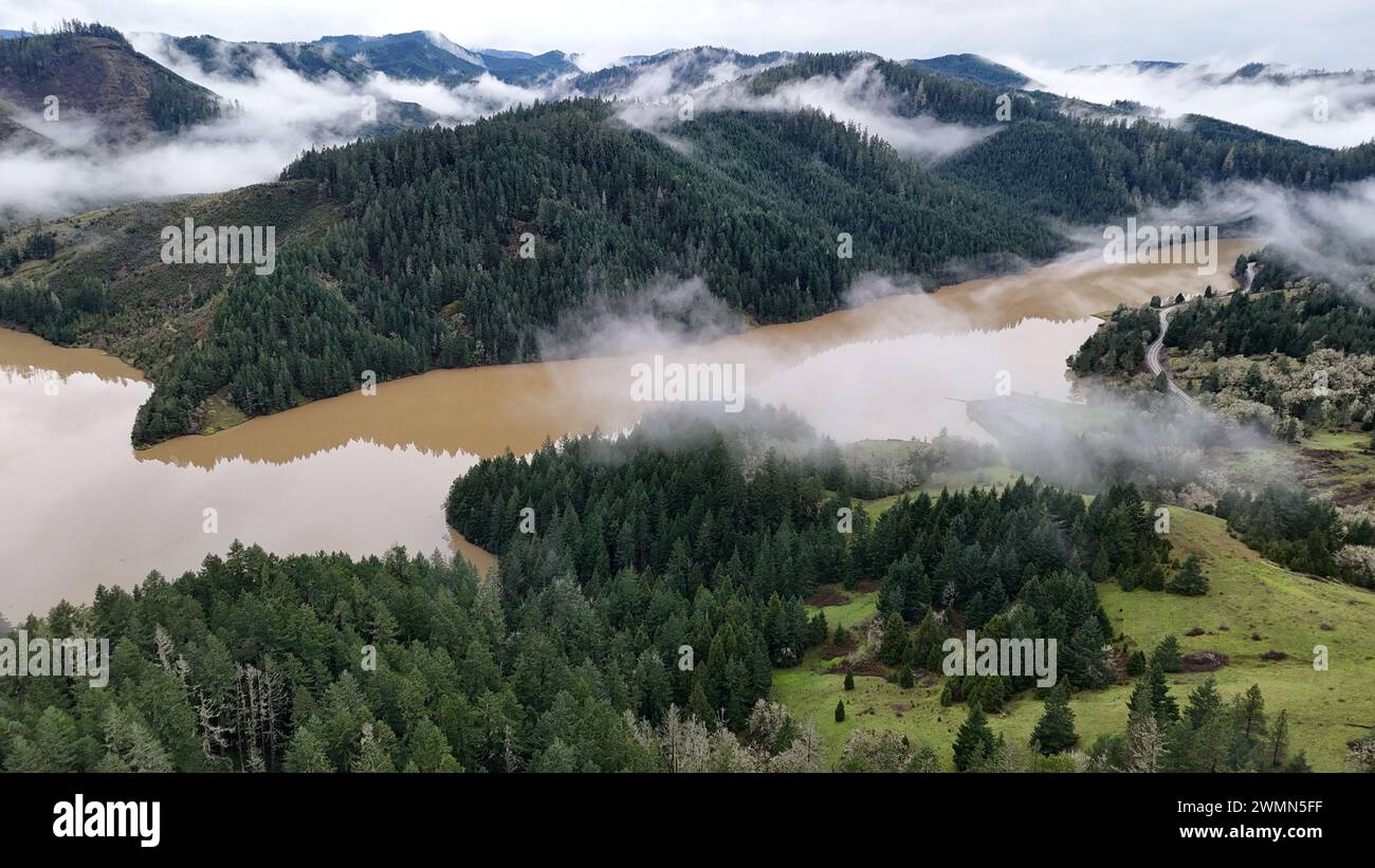 Una vista panoramica delle montagne nebbiose che si innalzano sopra un fiume marrone Foto Stock