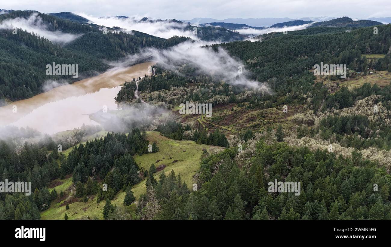 Una vista panoramica delle montagne nebbiose che si innalzano sopra un fiume marrone Foto Stock