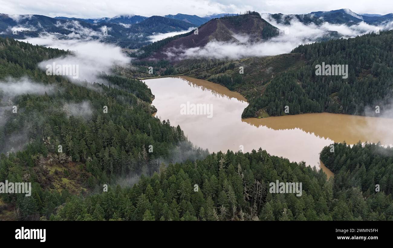 Una vista panoramica delle montagne nebbiose che si innalzano sopra un fiume marrone Foto Stock