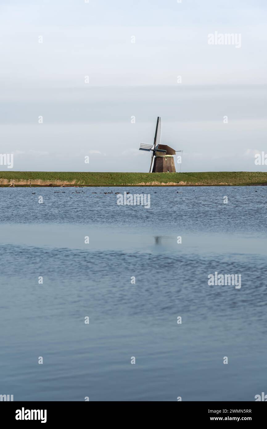 Tradizionale mulino solitario con tetto in paglia presso il lago Dutch a Dusk. Mezzo nascosto dietro una diga verdeggiante che si affaccia sulle acque tranquille di un prato allagato Foto Stock