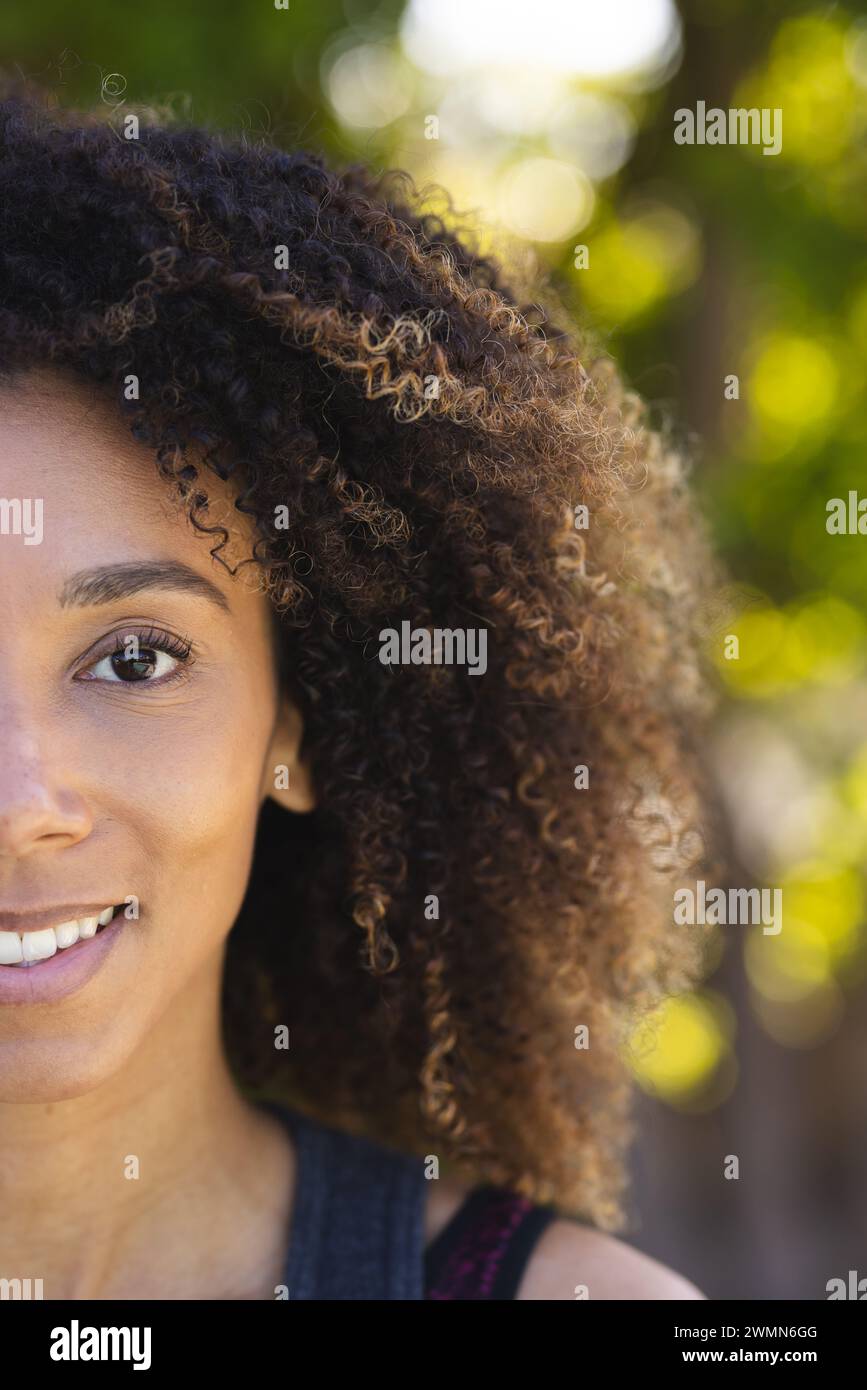 La donna birazziale sorride dolcemente all'aperto. La sua calda espressione completa lo sfondo naturale. Foto Stock