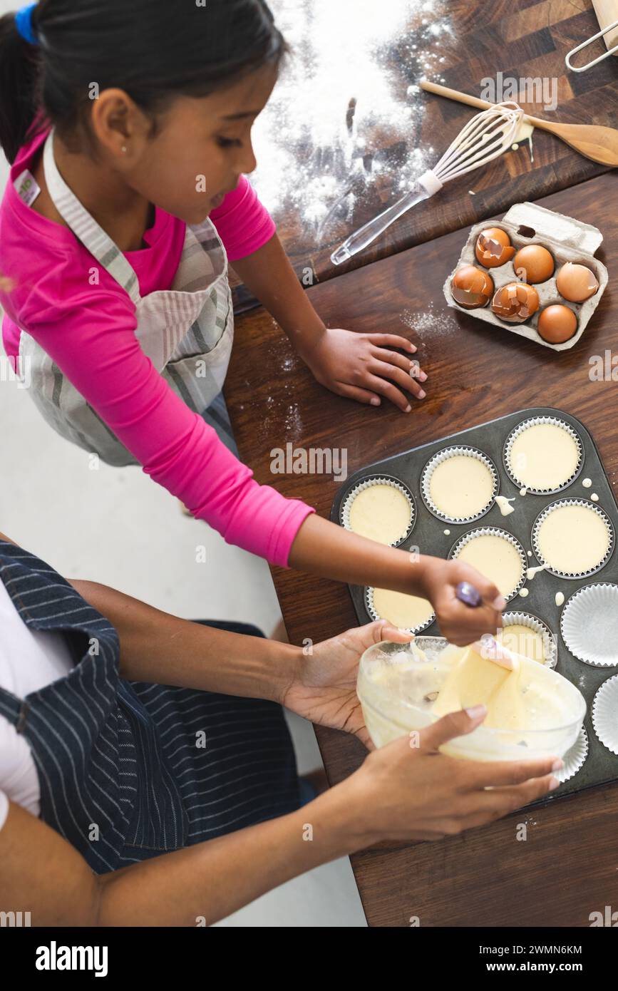 Ragazza birazziale che cuoce a casa per sua figlia, con spazio di copia. Sta imparando a fare i cupcake, creando un'esperienza divertente ed educativa. Foto Stock