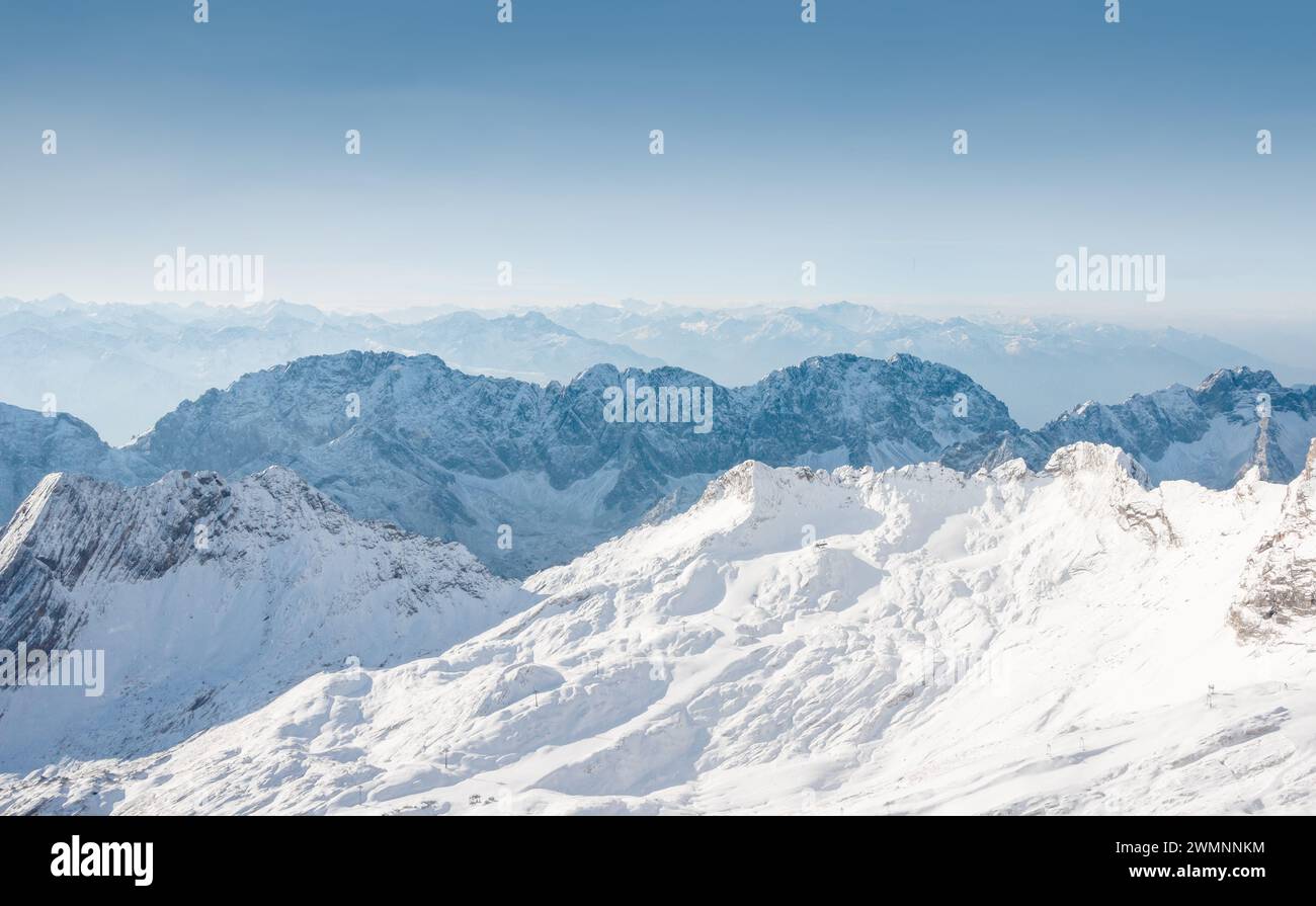 Montagne blu fredde in una giornata di sole - immagine retroilluminata con silhouette di cime. Cima innevata della catena montuosa di Wetterstein. Foto Stock