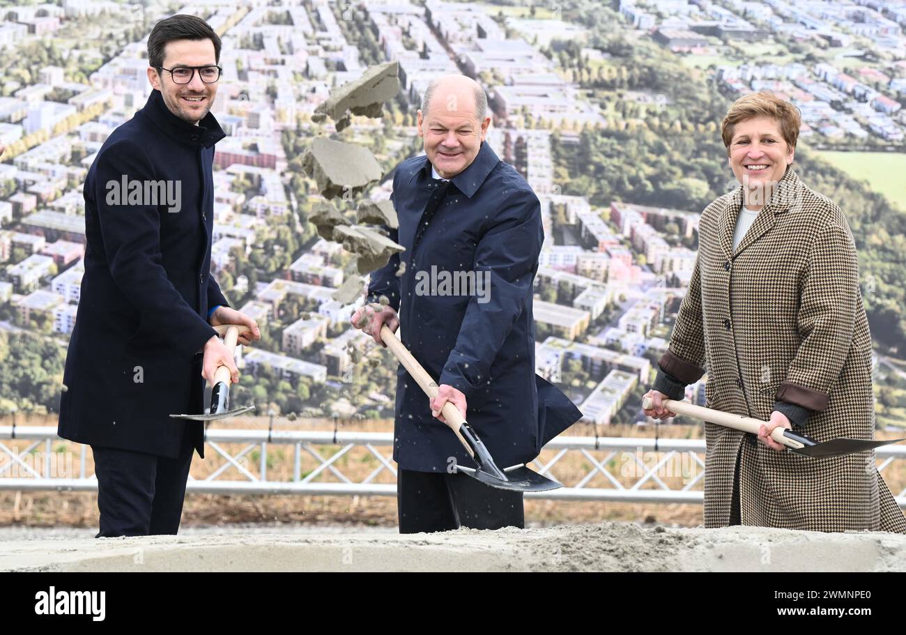 Friburgo, Germania. 27 febbraio 2024. Martin Horn (l-r), Lord sindaco della città di Friburgo, Cancelliere Olaf Scholz (SPD) e Nicole Razavi (CDU), Ministro dell'edilizia abitativa e dello sviluppo regionale del Baden-Württemberg, pala la terra di fronte a uno striscione con un'immagine computerizzata del progetto di costruzione durante una cerimonia di inaugurazione del nuovo grande quartiere Dietenbach di Friburgo. Crediti: Bernd Weißbrod/dpa/Alamy Live News Foto Stock