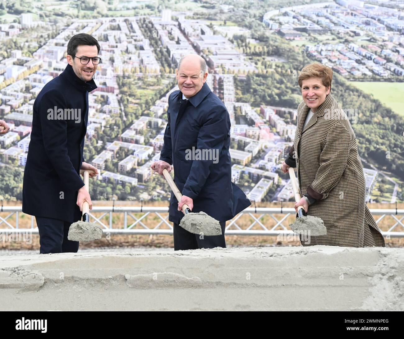 Friburgo, Germania. 27 febbraio 2024. Martin Horn (l-r), Lord sindaco della città di Friburgo, Cancelliere Olaf Scholz (SPD) e Nicole Razavi (CDU), Ministro dell'edilizia abitativa e dello sviluppo regionale del Baden-Württemberg, pala la terra di fronte a uno striscione con un'immagine computerizzata del progetto di costruzione durante una cerimonia di inaugurazione del nuovo grande quartiere Dietenbach di Friburgo. Crediti: Bernd Weißbrod/dpa/Alamy Live News Foto Stock