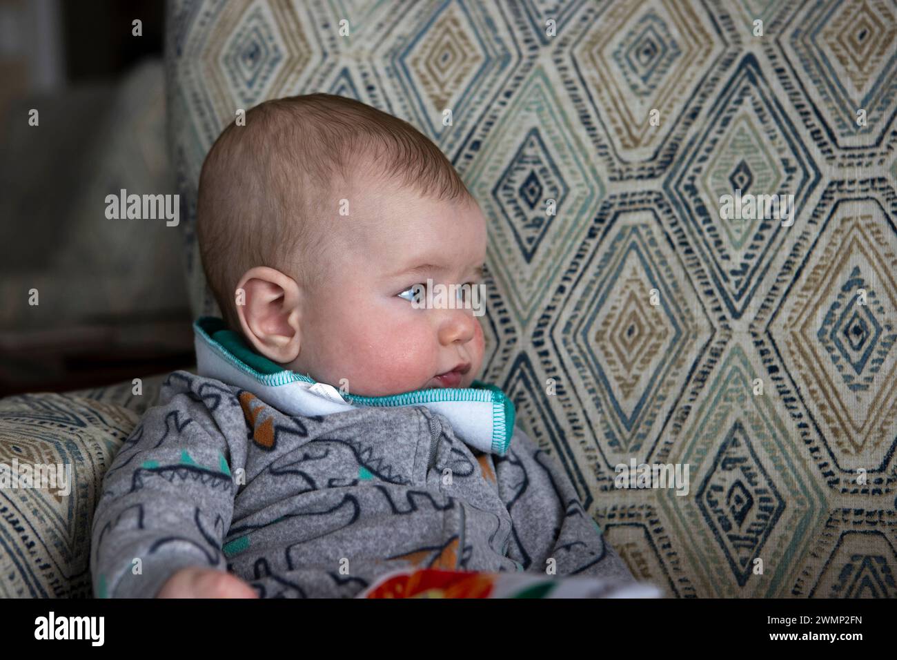 Bambino di quattro mesi appoggiato su una sedia guardando di lato. Foto Stock