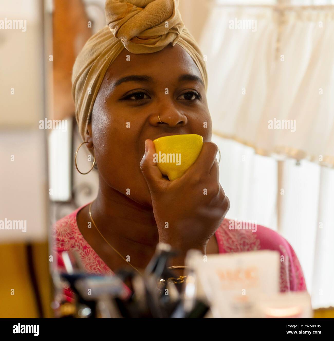 Una ragazza succhia un limone giallo davanti allo specchio. Si guarda e fa schifo. Foto Stock