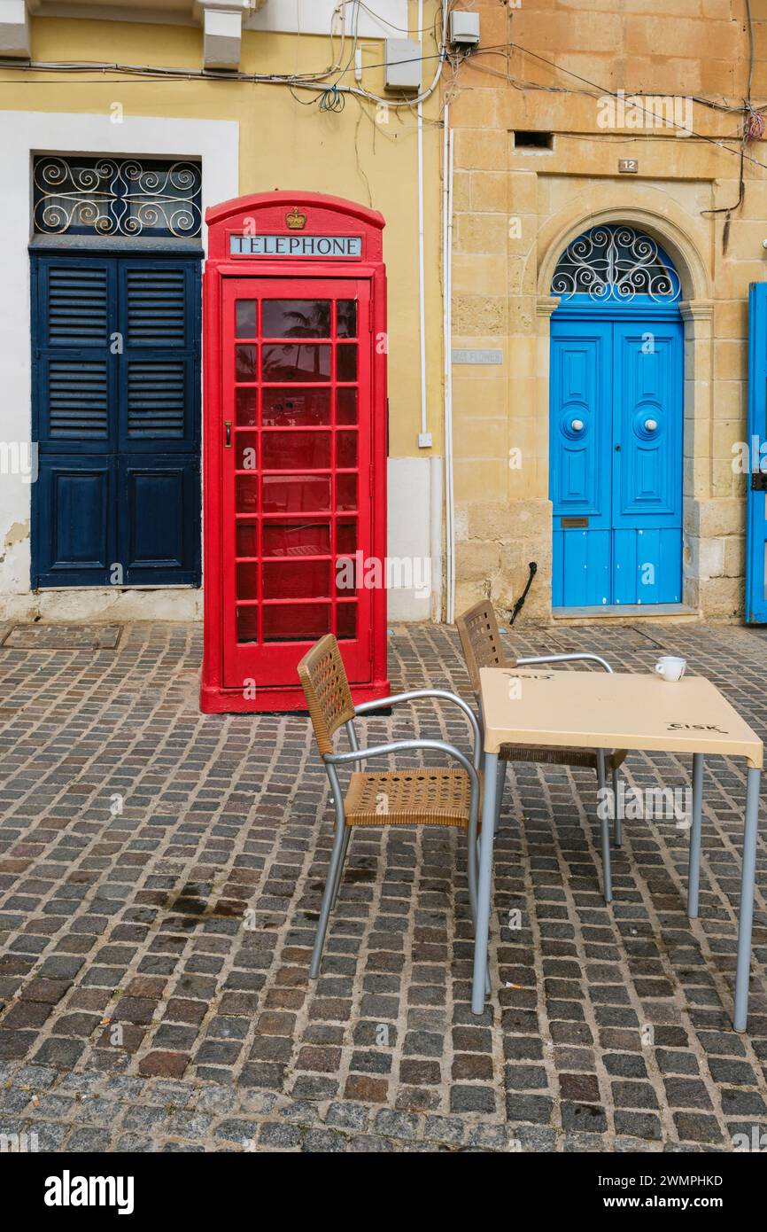 Una vecchia scatola telefonica in stile britannico e una porta blu colorata in Piazza Marsaxlokk, Marsaxlokk, Malta Foto Stock