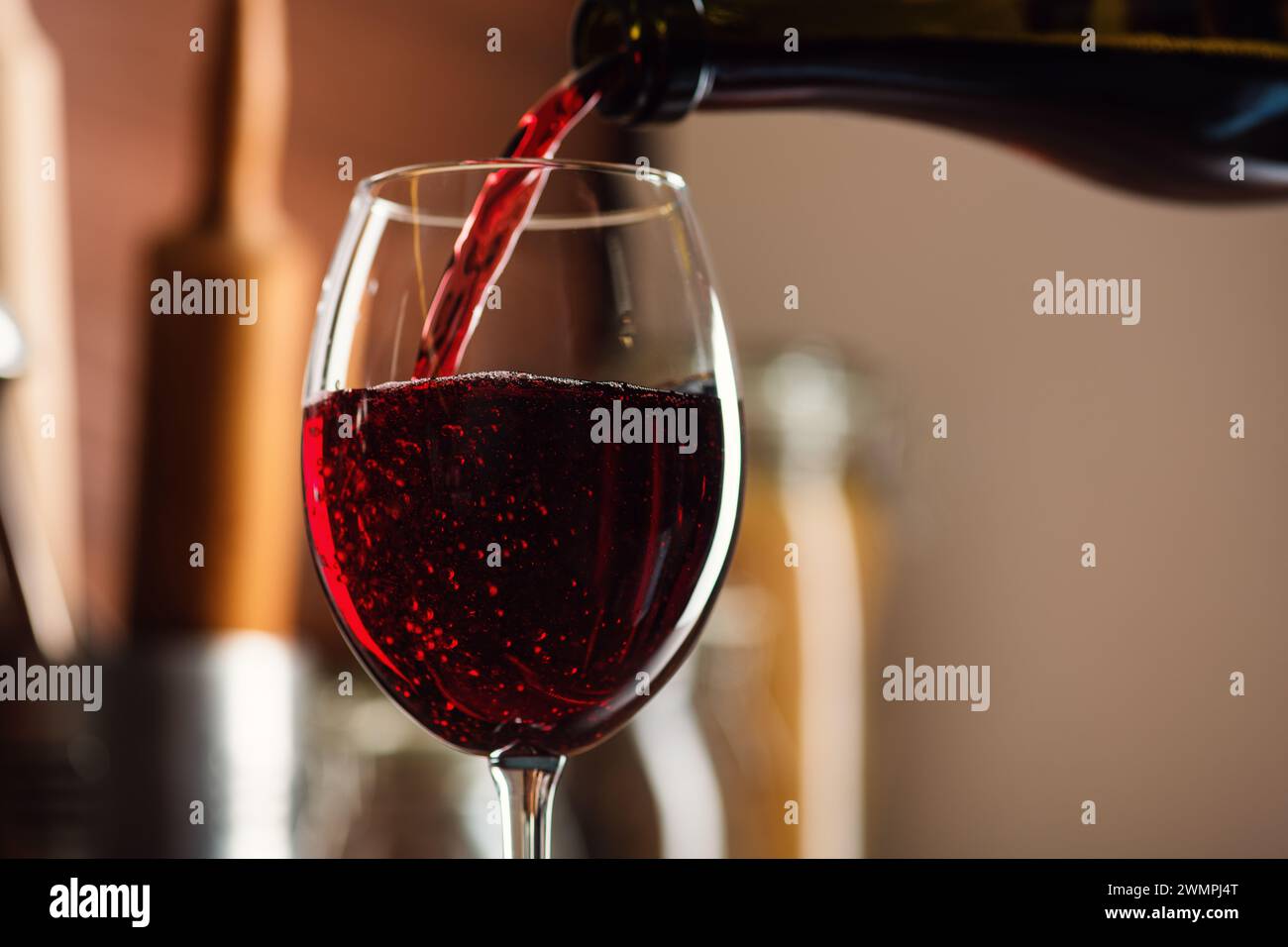 Vino rosso francese che si versa in un bicchiere di bollicine con uno spruzzo sul tavolo in cucina, uno shot di alta qualità Foto Stock