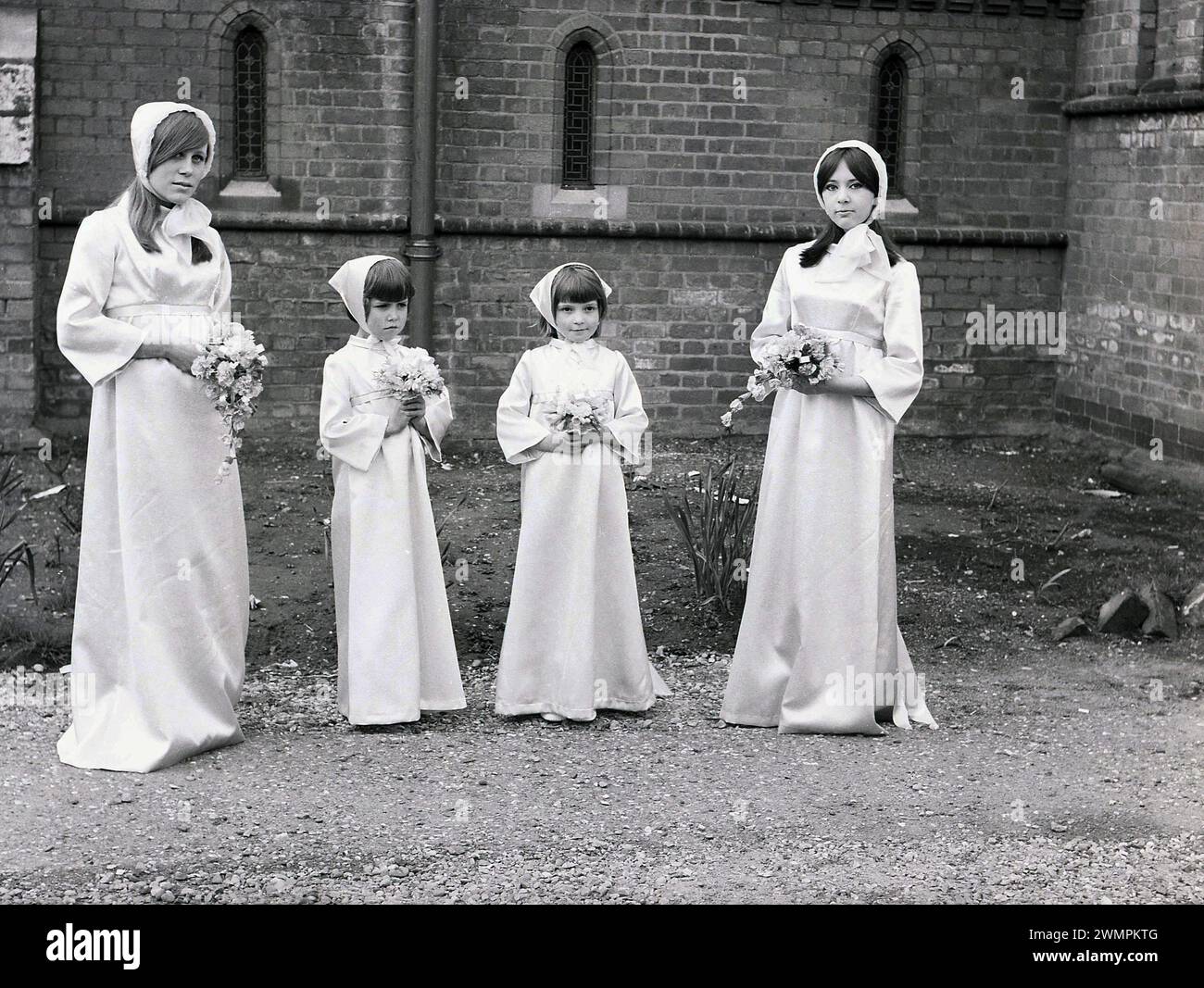 Anni '1960, storico, quattro damigelle, due giovani donne e due bambine in piedi con i loro lunghi abiti e copricapo su un sentiero fuori da una chiesa, Inghilterra, Regno Unito. Foto Stock