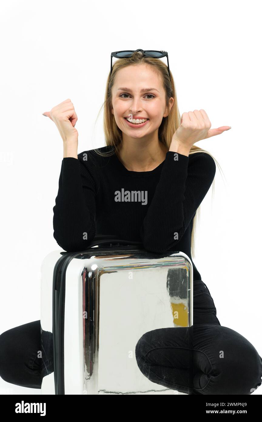 Bella giovane donna con valigia su sfondo bianco. Ragazza in abiti neri. Foto Stock