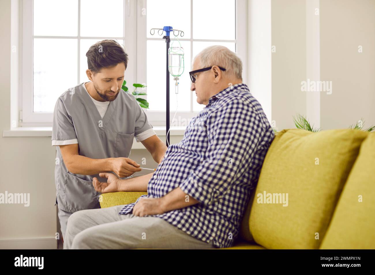 Operatore sanitario maschile che prepara pazienti anziani per la terapia IV a casa Foto Stock