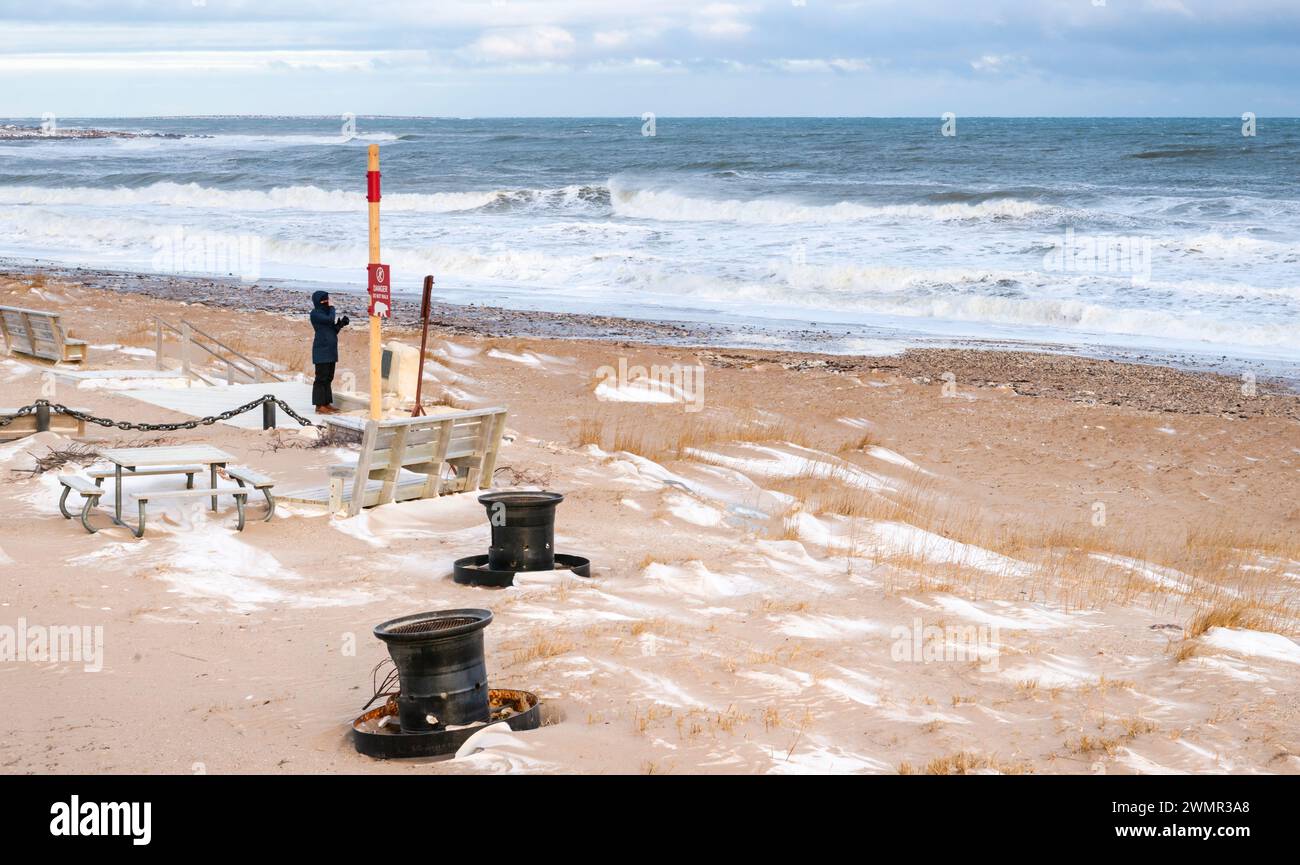 Un turista visita la spiaggia della Baia di Hudson, in piedi vicino a un cartello che avverte gli orsi polari vicino alla città di Churchill, Manitoba, Canada Foto Stock