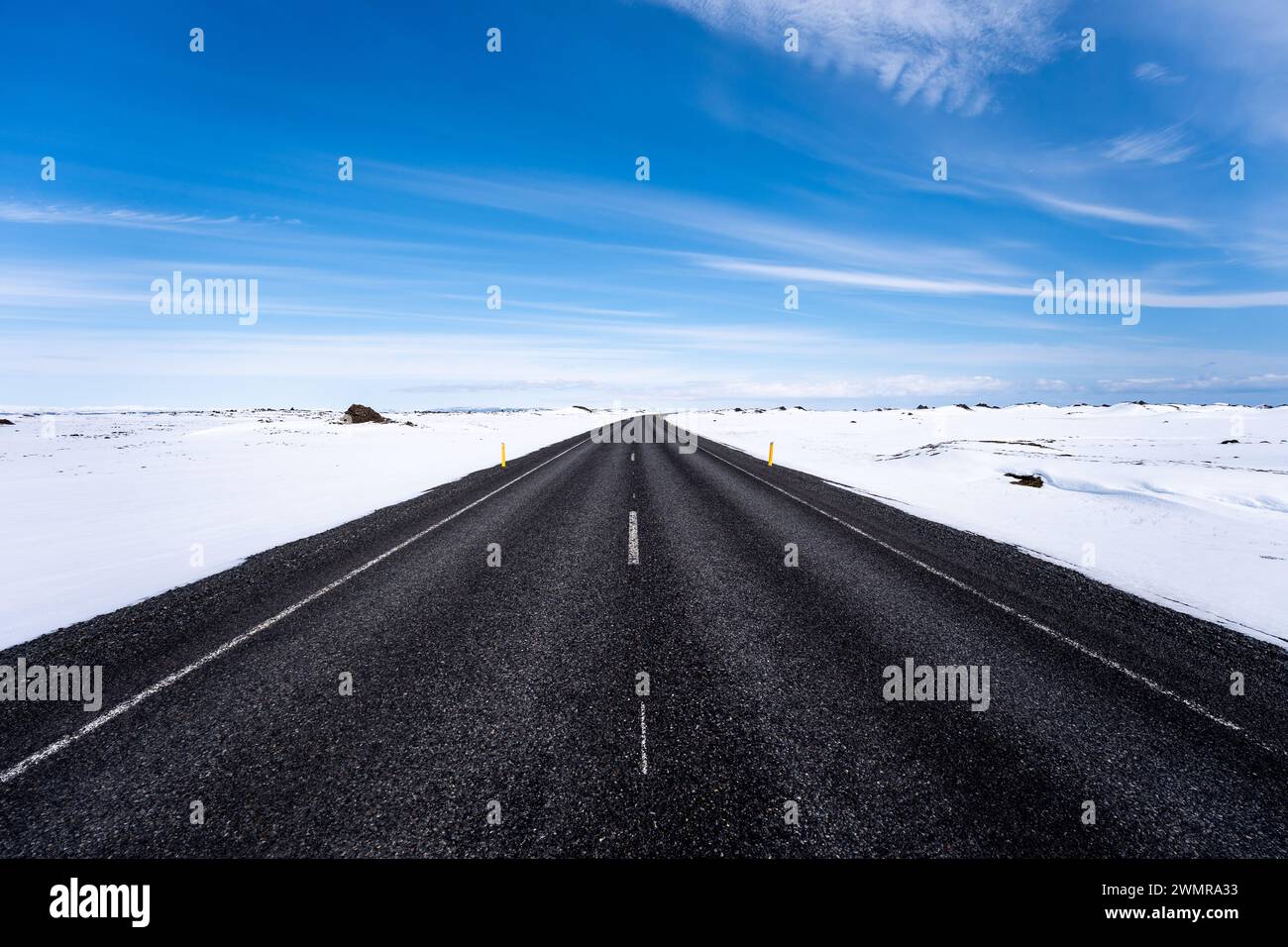 Solitaria strada asfaltata nera con neve sulla spalla in Islanda Foto Stock