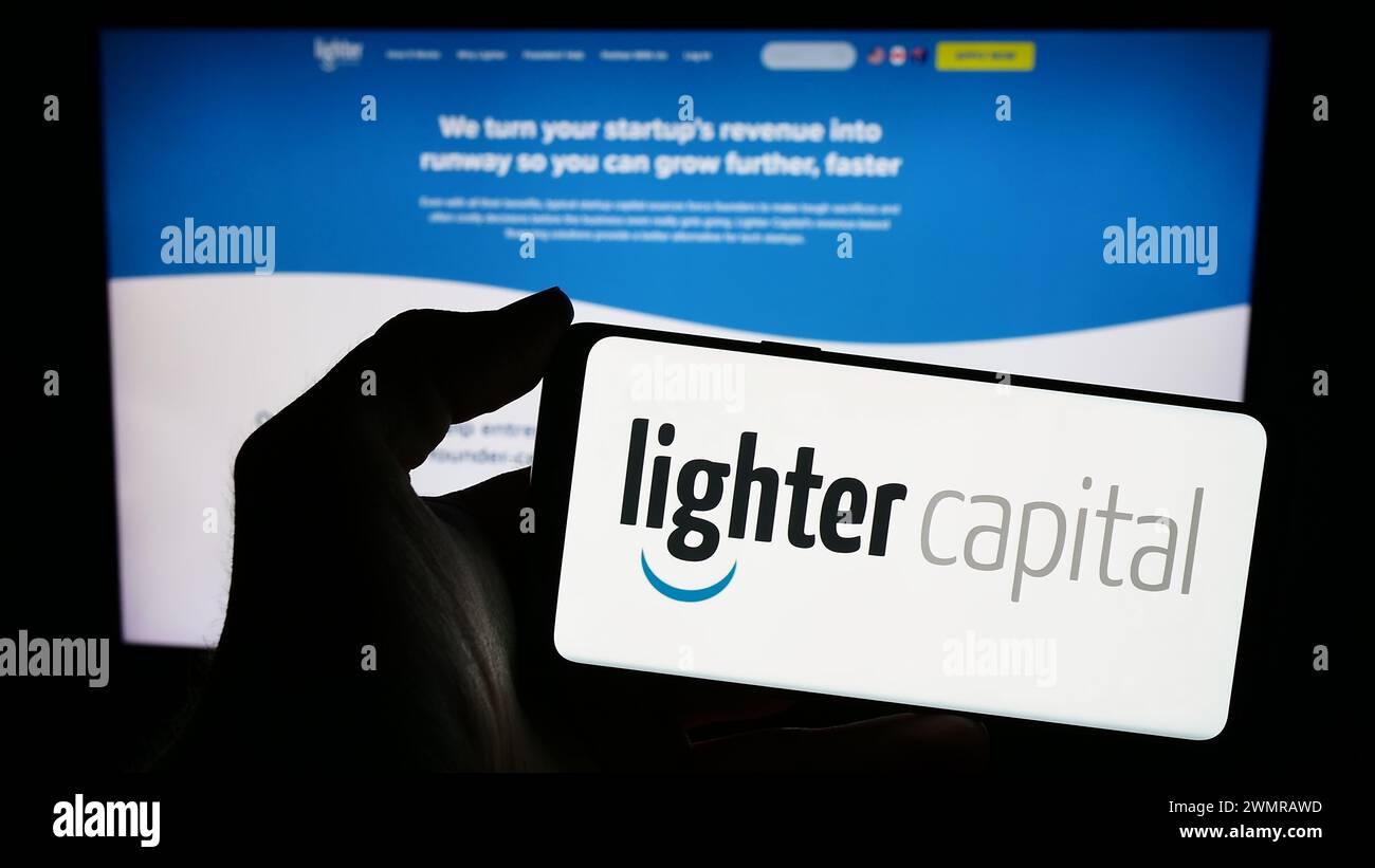 Persona con smartphone con logo della società statunitense di servizi finanziari Lighter Capital Inc. Davanti al sito Web. Mettere a fuoco il display del telefono. Foto Stock