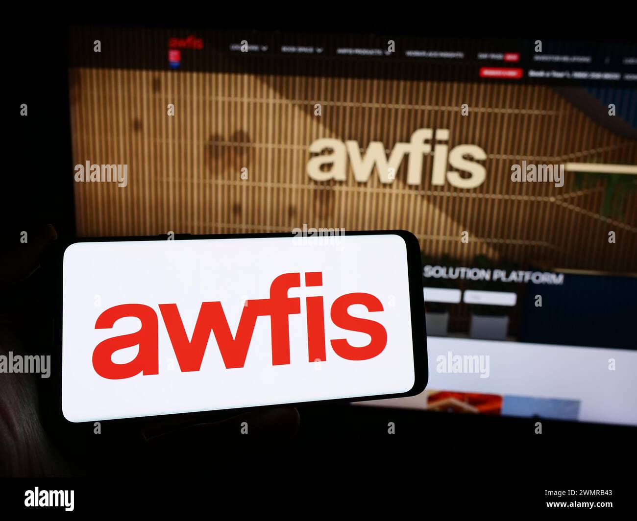 Persona che detiene un telefono cellulare con il logo della società indiana Awfis Space Solutions Limited, situata di fronte alla pagina Web. Mettere a fuoco il display del telefono. Foto Stock