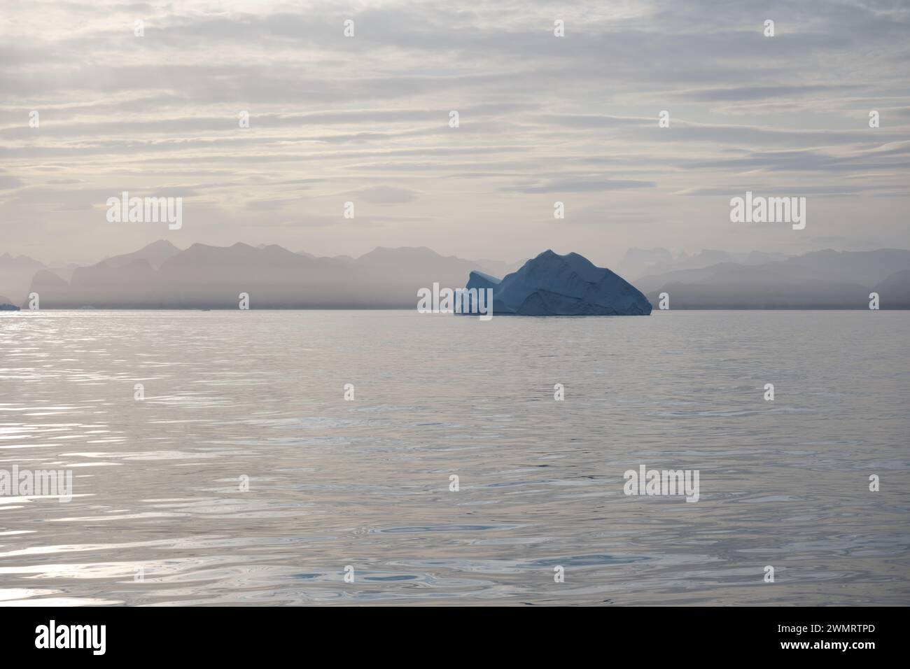 L'iceberg galleggia nei mari dorati mentre il sole tramonta diffondendo luce dorata sulle montagne e sui ghiacci della Groenlandia orientale. Foto Stock