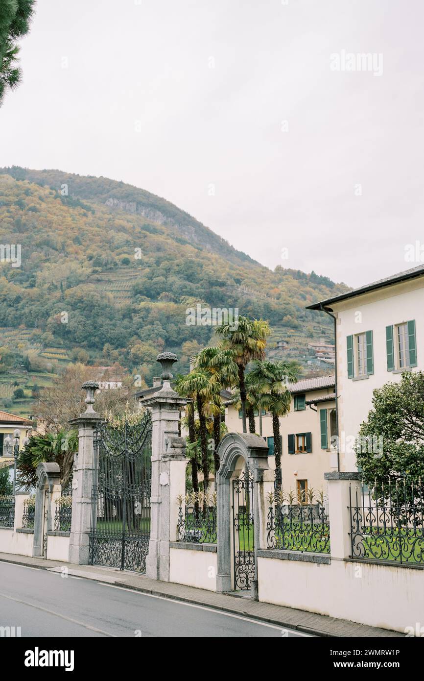 Ville costose dietro recinzioni in ferro battuto ai piedi delle montagne. Lago di Como, Italia Foto Stock
