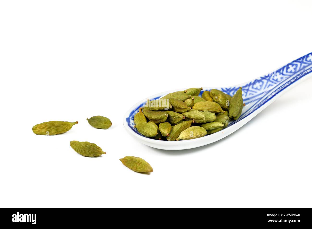 Un cucchiaio da zuppa di cialde di Cardamomo verde essiccate (Elettaria cardamomum) isolate su fondo bianco. ritaglio per uso illustrativo e editoriale. Foto Stock