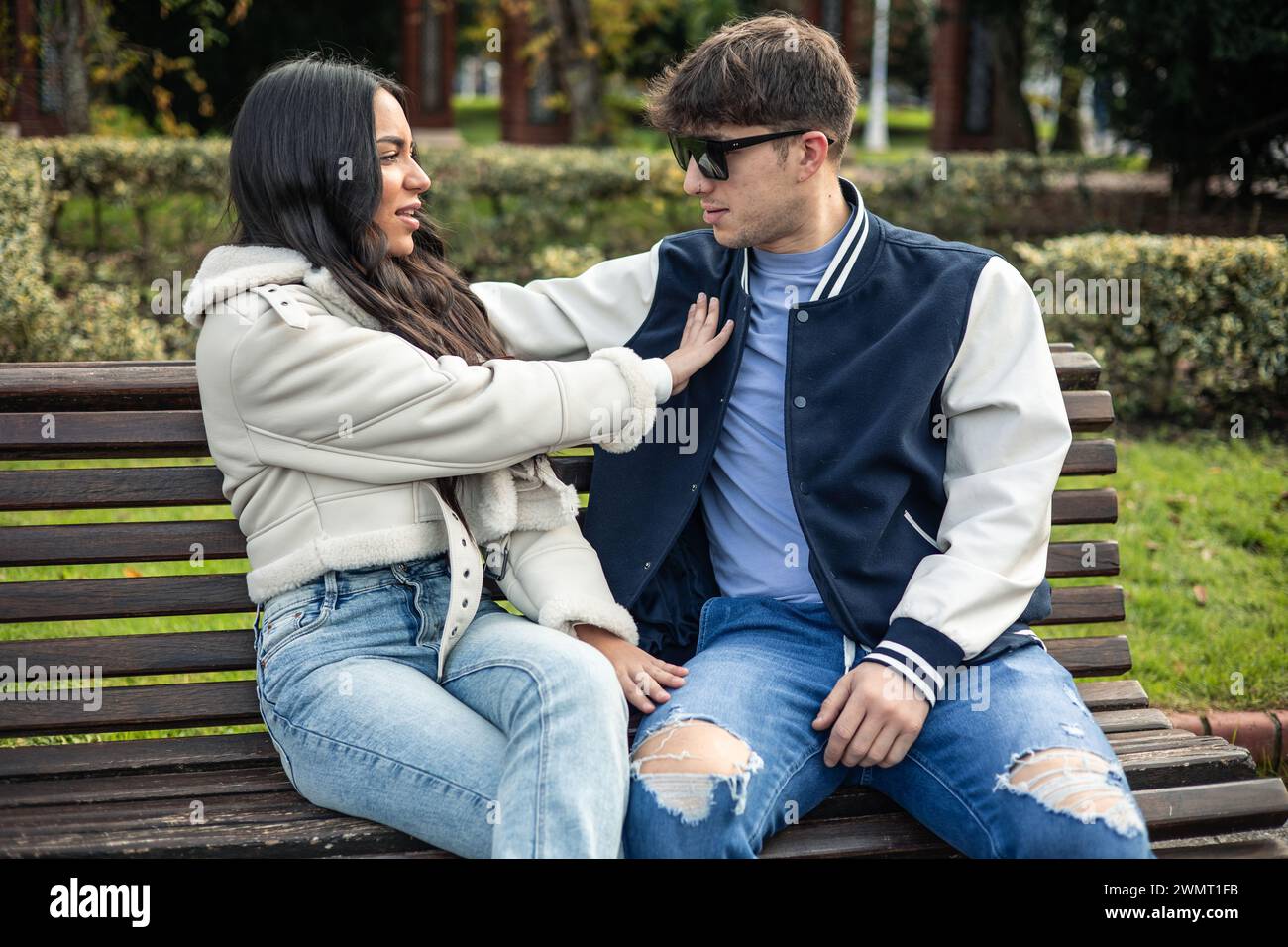 Arrabbiata studentessa latina che rifiuta il suo ragazzo caucasico seduto su una panchina all'aperto Foto Stock