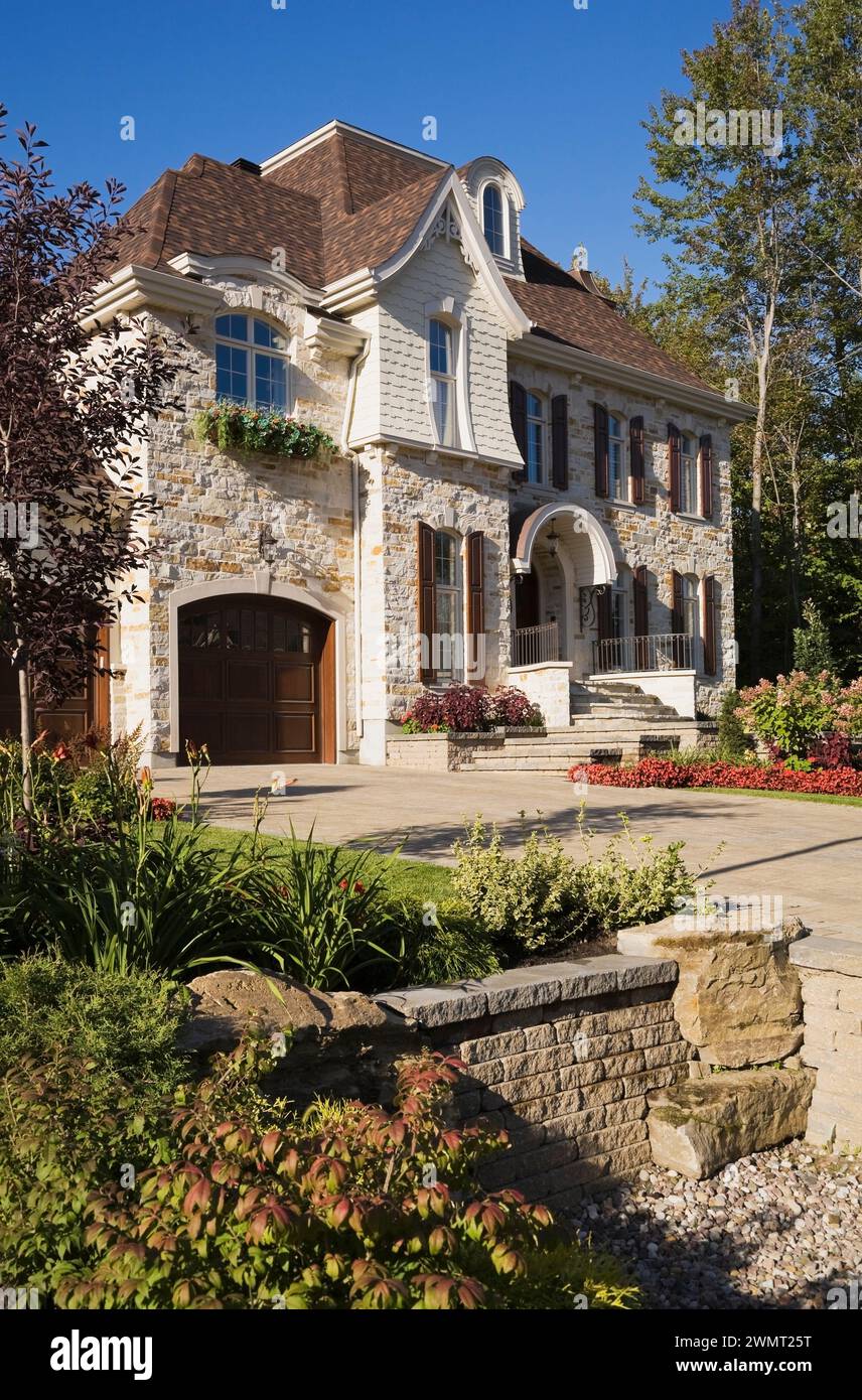 Lussuosa casa a due piani con abbronzatura marrone e pietra tagliata con due garage per auto, vialetto di pietra e giardino panoramico in estate. Foto Stock