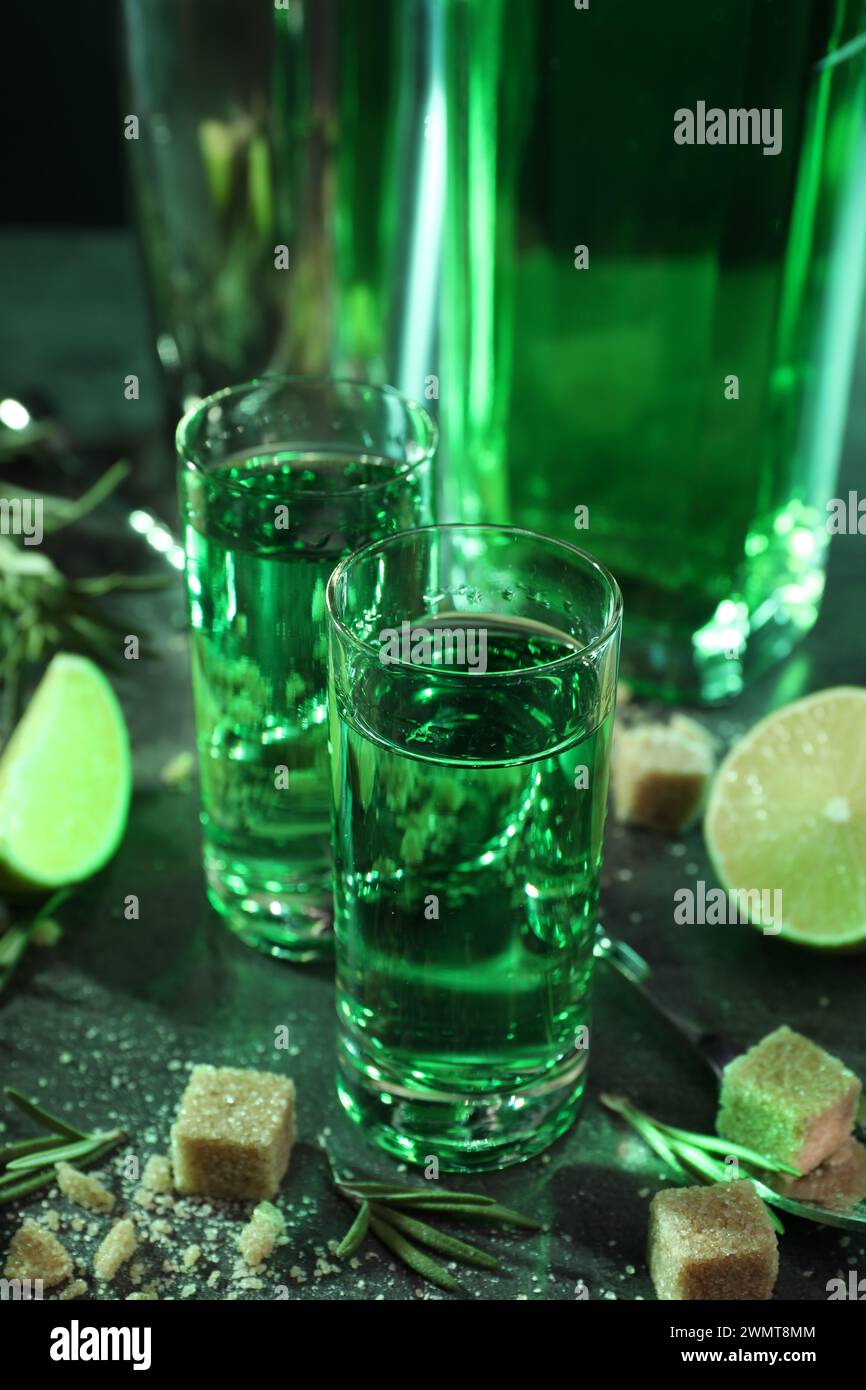 Absinthe in bicchieri da shot, zucchero di canna, lime e rosmarino su tavolo grigio, primo piano. Bevanda alcolica Foto Stock