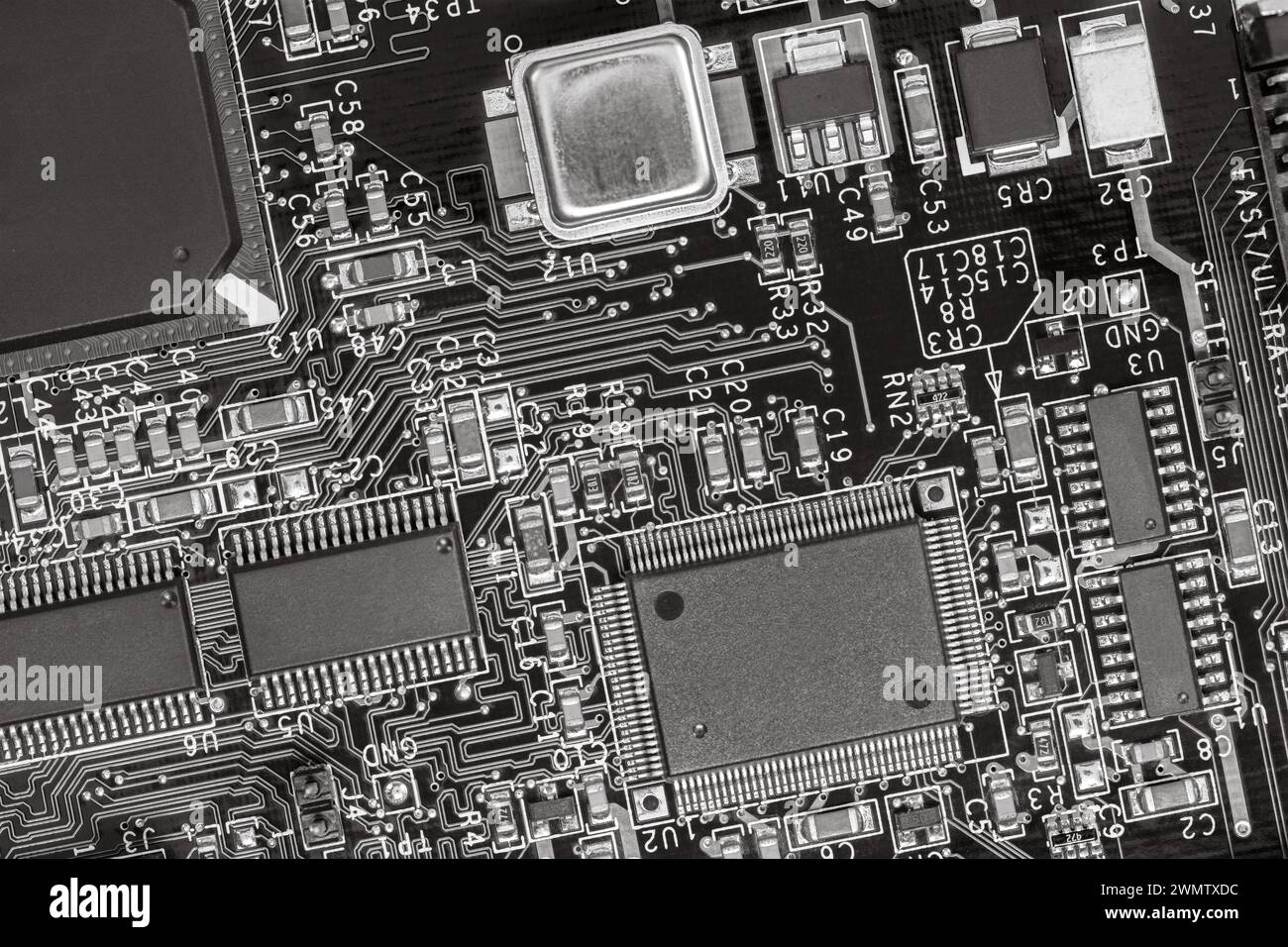 primo piano di una scheda a circuito stampato con resistori, condensatori, microchip e componenti elettronici. b/w. Foto Stock