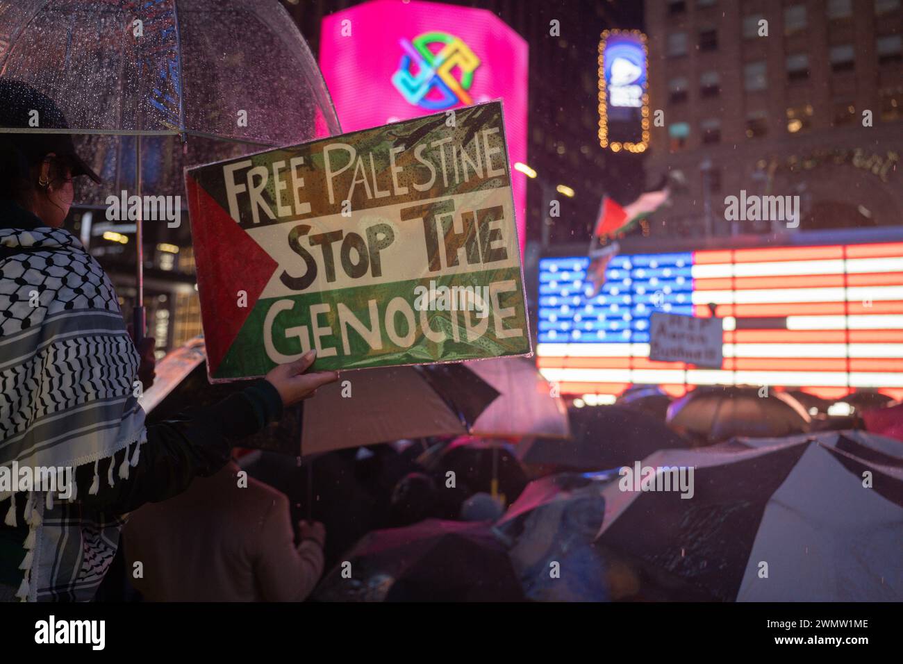 Manhattan, Stati Uniti. 27 febbraio 2024. Un manifestante ha un cartello con scritto "Free Palestine Stop the Genocide" scritto sulla bandiera della Palestina durante una veglia per l'aviatore statunitense Aaron Bushnell. Il membro delle forze armate statunitensi si è autoimmolato fuori dall'ambasciata israeliana a Washington, DC domenica in segno di protesta per il conflitto in corso in Palestina e per la continuazione dell'offensiva da parte di Israele. Credito: SOPA Images Limited/Alamy Live News Foto Stock