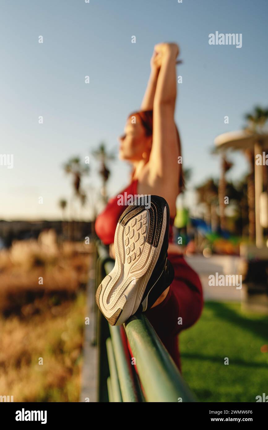 Una giovane donna si impegna in una routine dinamica di stretching nelle ore dorate del mattino, sottolineando l'importanza della flessibilità in un regime di fitness. Foto Stock