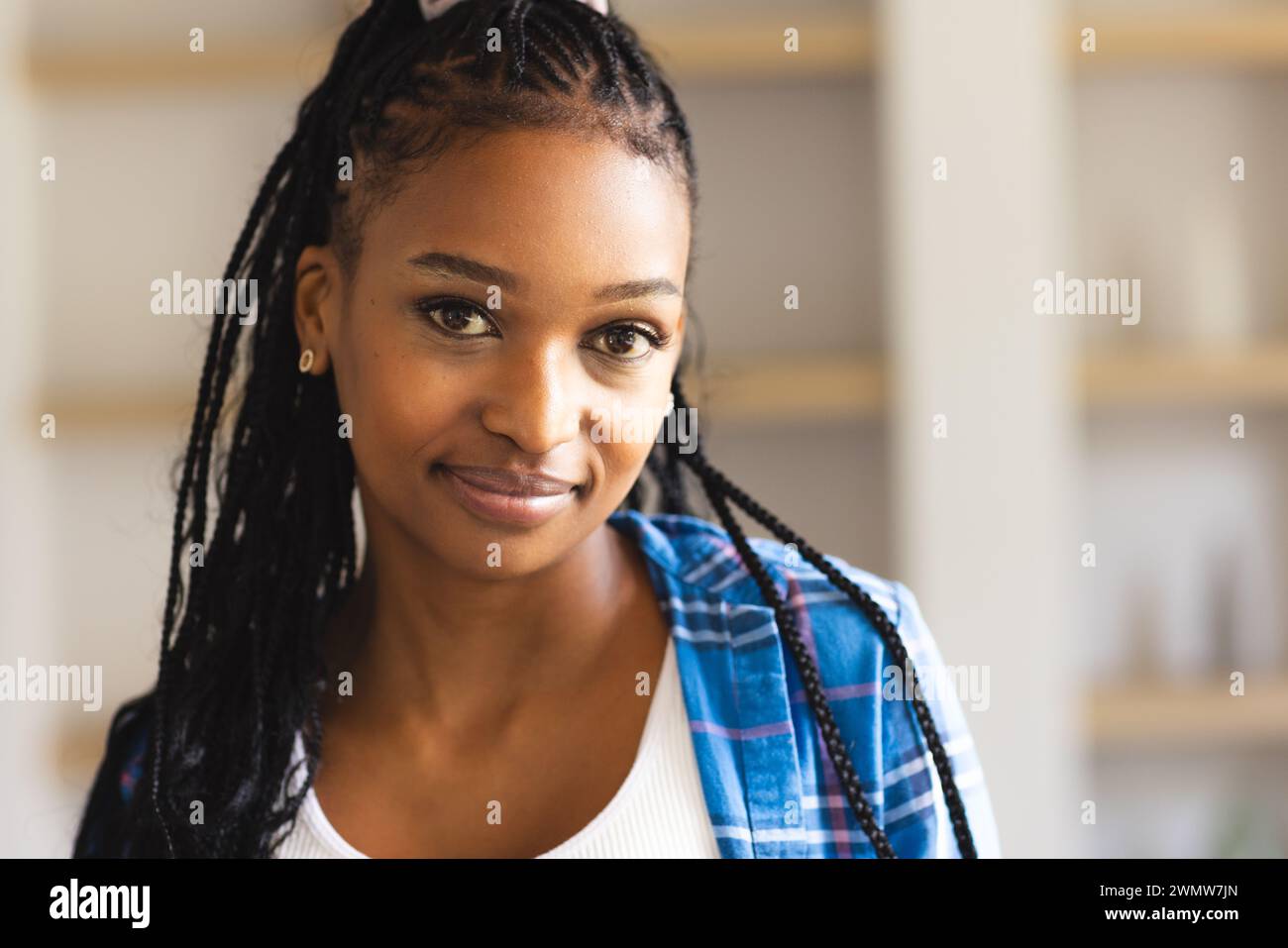 Una giovane donna afroamericana con i capelli intrecciati sorride dolcemente alla telecamera Foto Stock