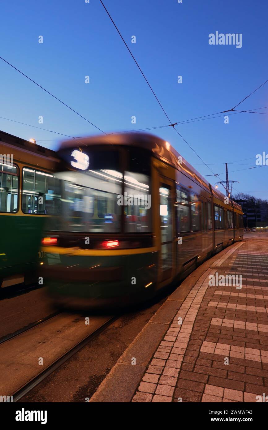 Il tram parte da una fermata del tram nell'ora blu di una mattinata limpida, vista posteriore, lunga esposizione. Foto Stock
